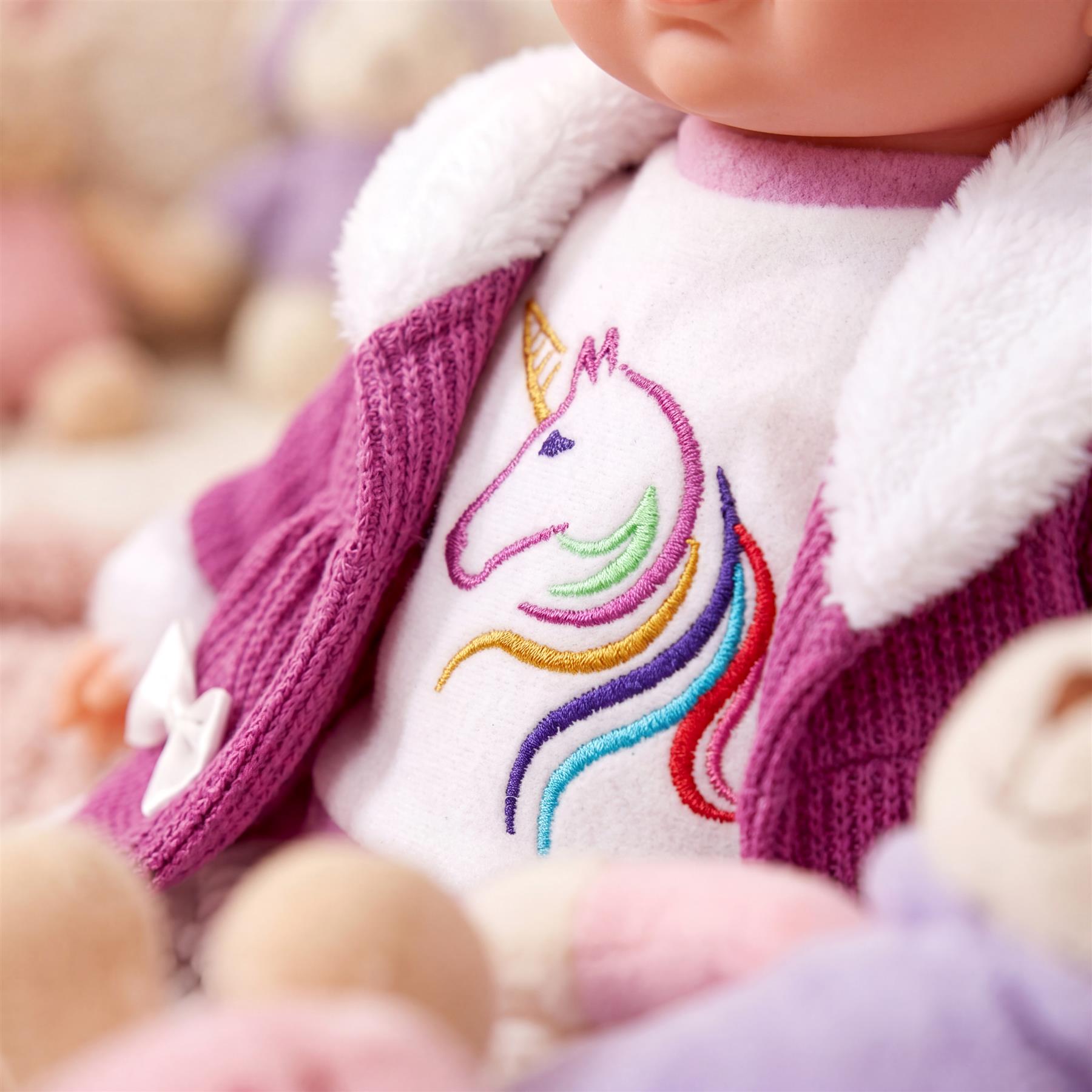 A doll wears a purple coat with a fuzzy white collar over a white top featuring a colorful unicorn embroidery.