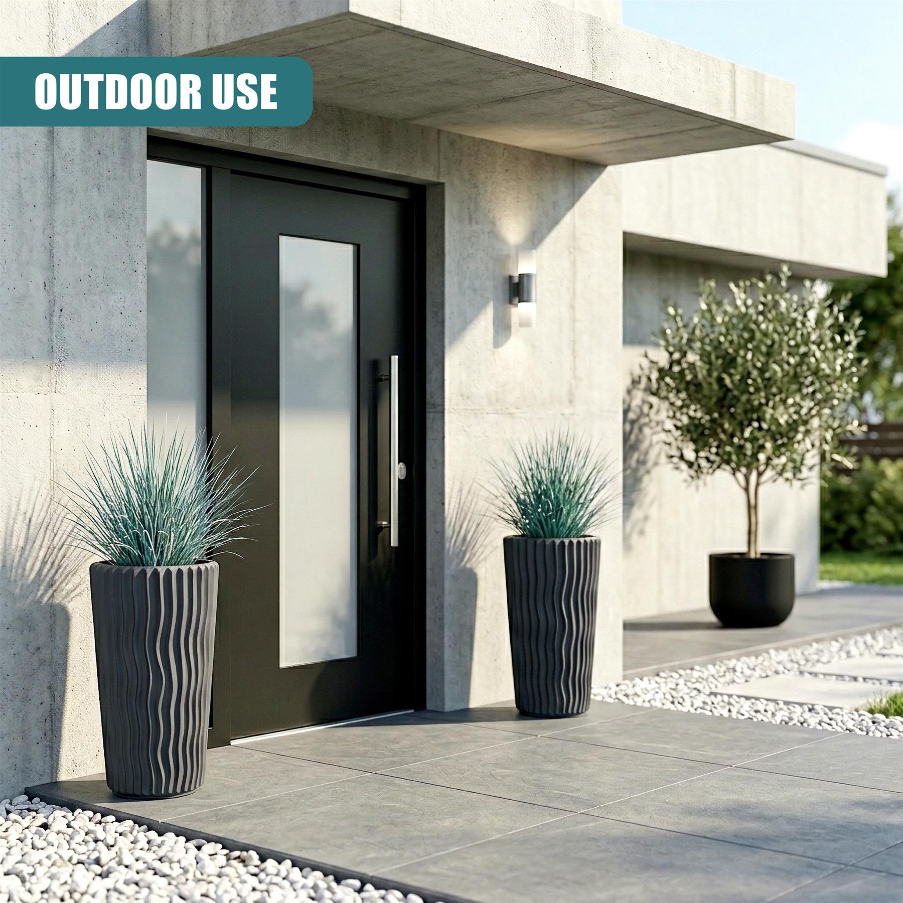 Two tall, dark gray, ribbed planters with green foliage flank a modern concrete entryway door.