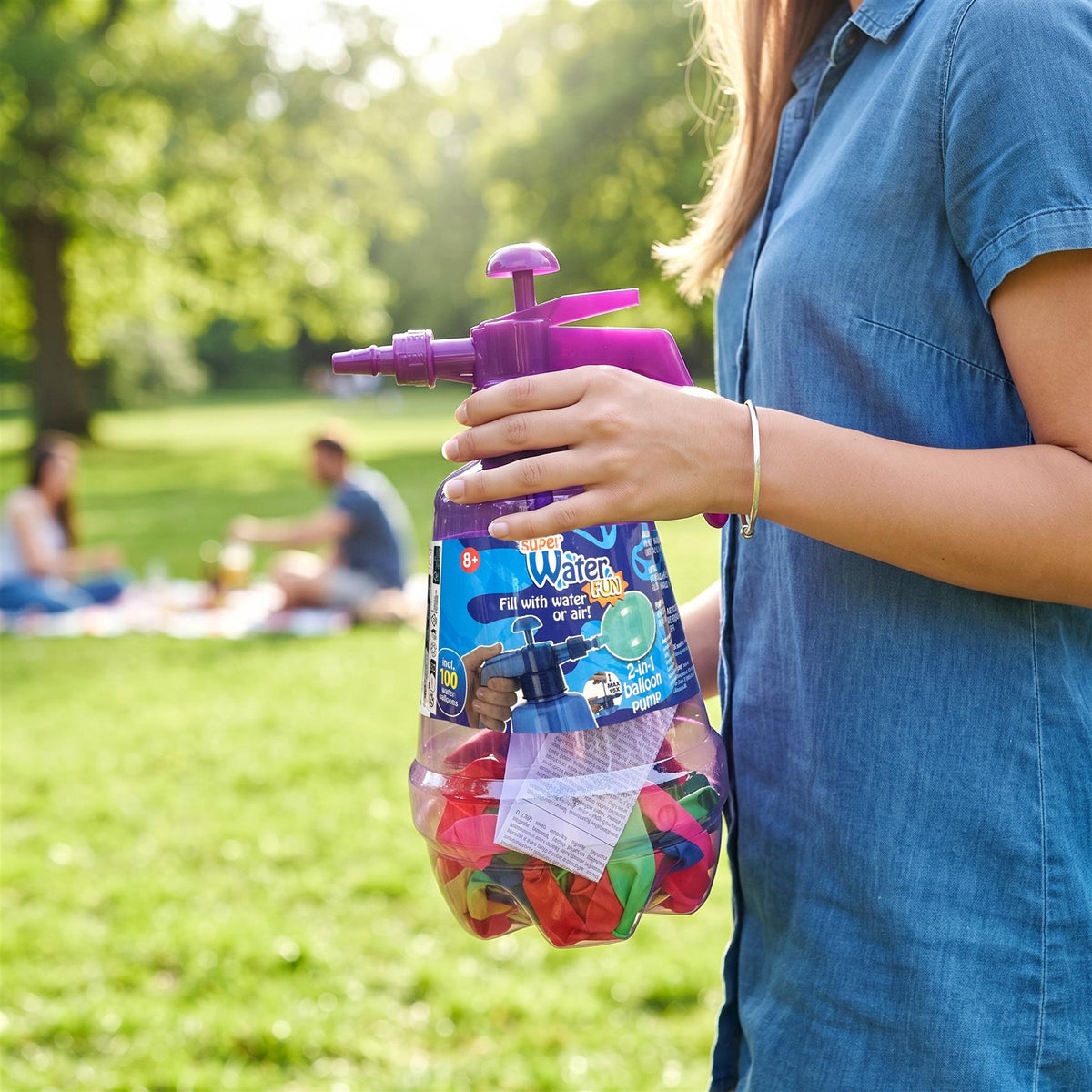 A woman holds a purple 2 in 1 Air & Water Balloon Pump bottle with 100 balloons in a park
