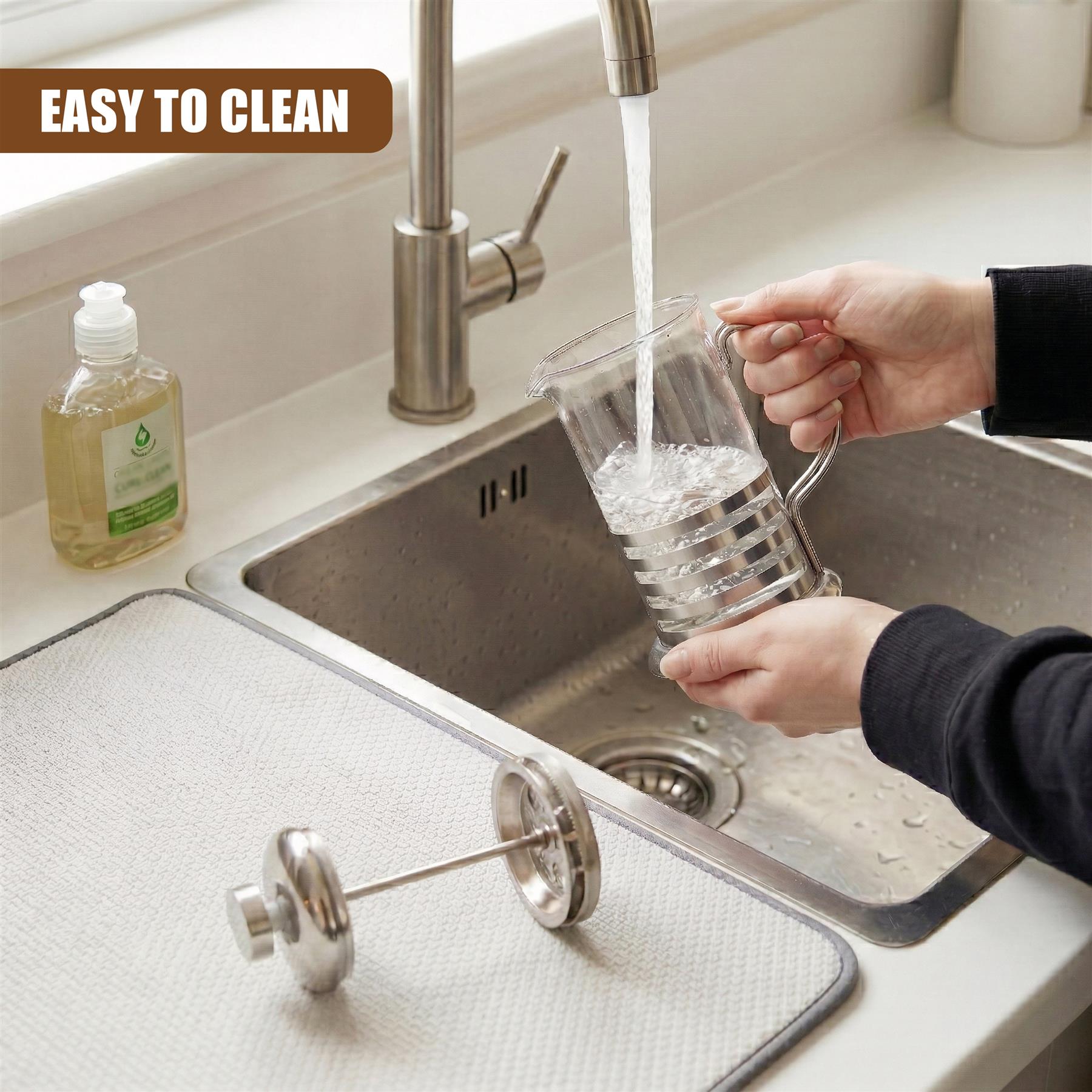 Hands fill a clear glass carafe from a kitchen faucet over a stainless steel sink.