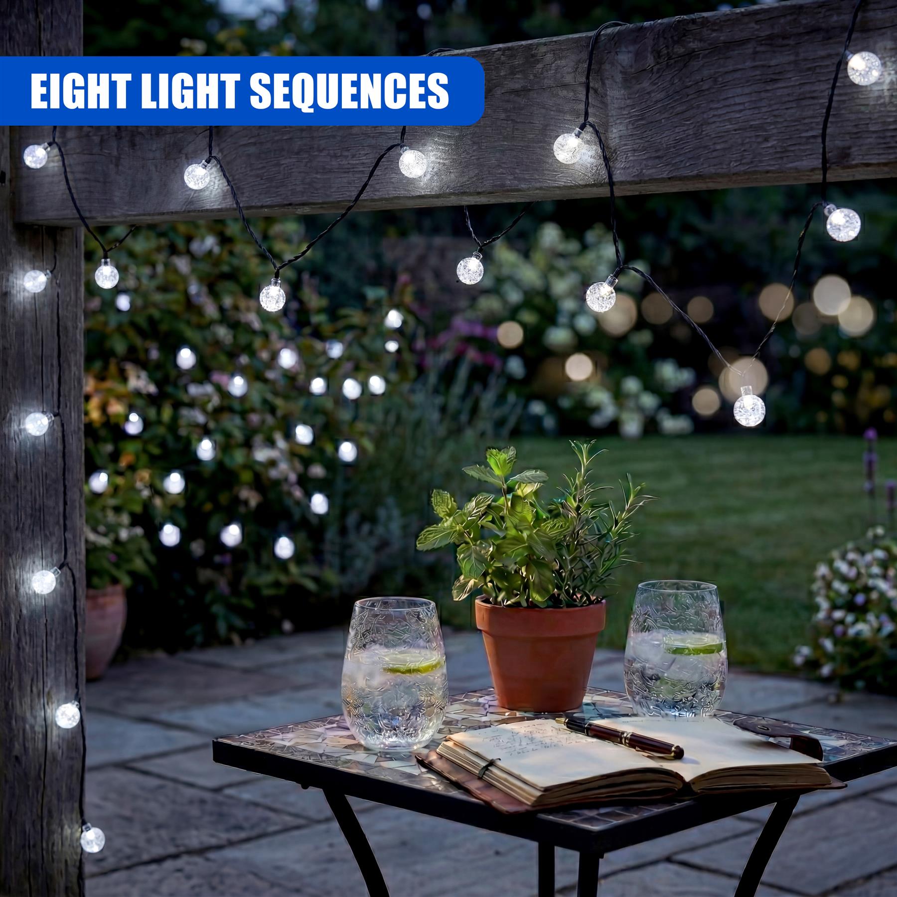 Solar string lights hang from a wooden arbor above a table displaying books, glass spheres, and potted plants.