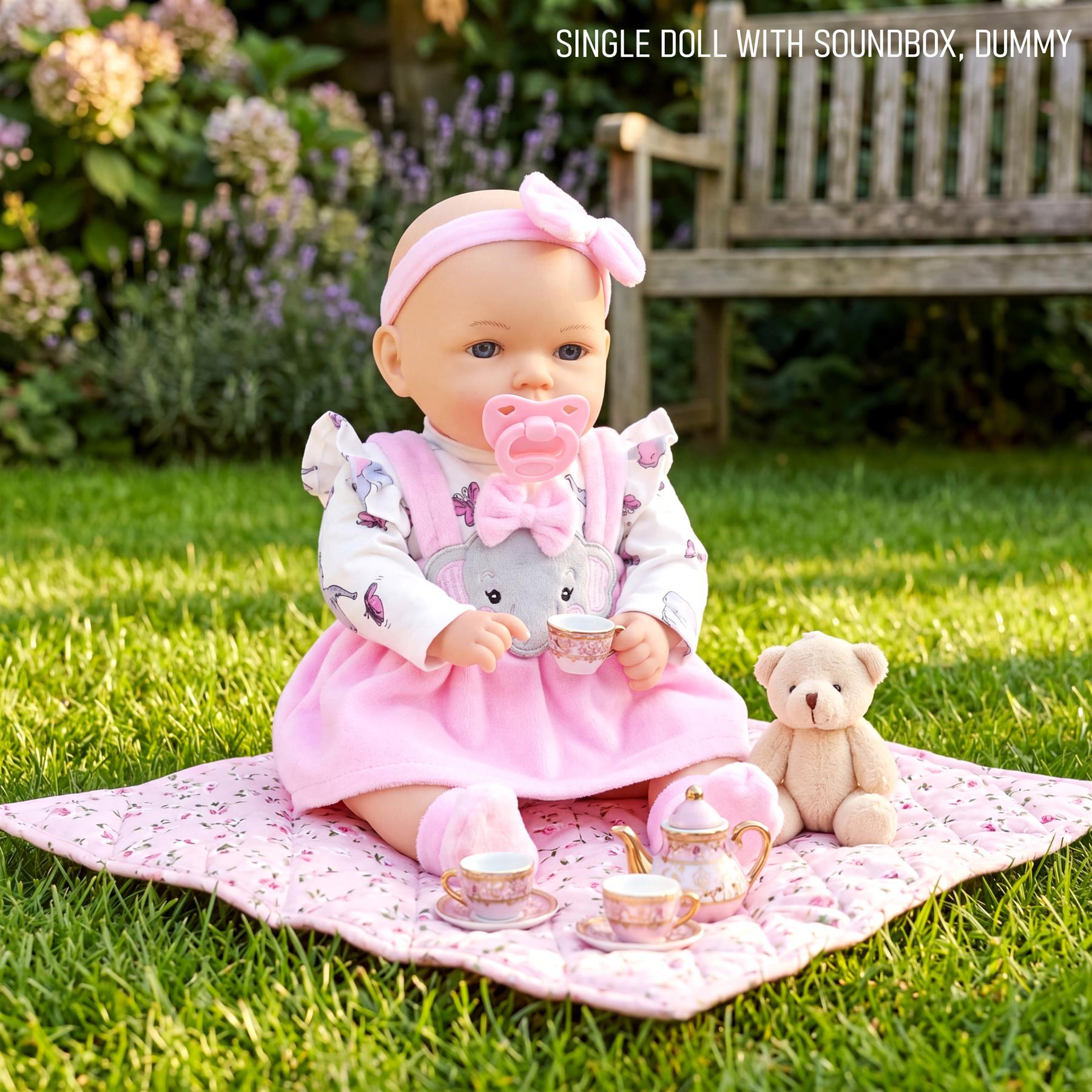 Blonde doll sits on a pink blanket with a miniature tea set and stuffed teddy bear.