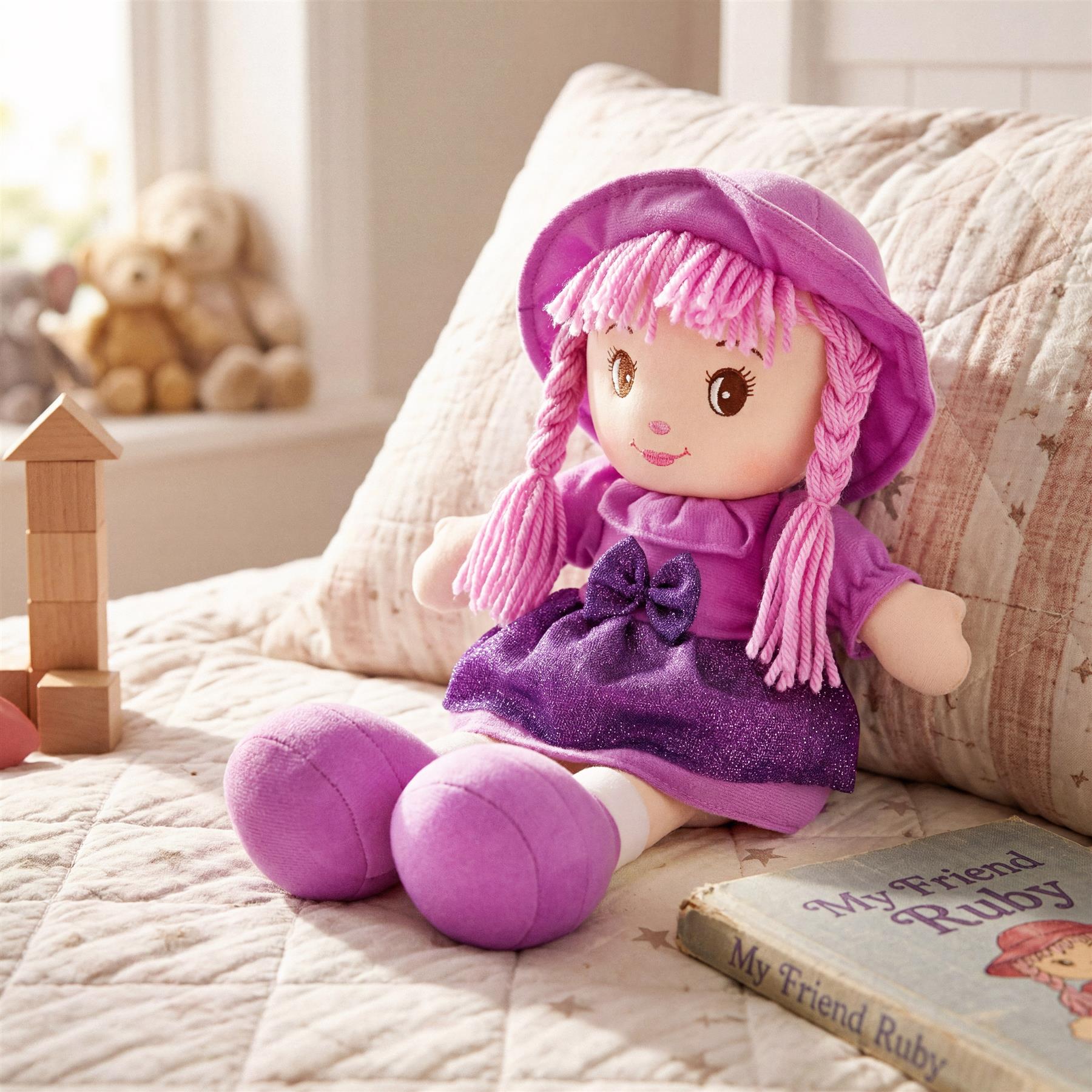 The rag doll Ruby, dressed in purple, lies on a cushion next to blocks and a book.
