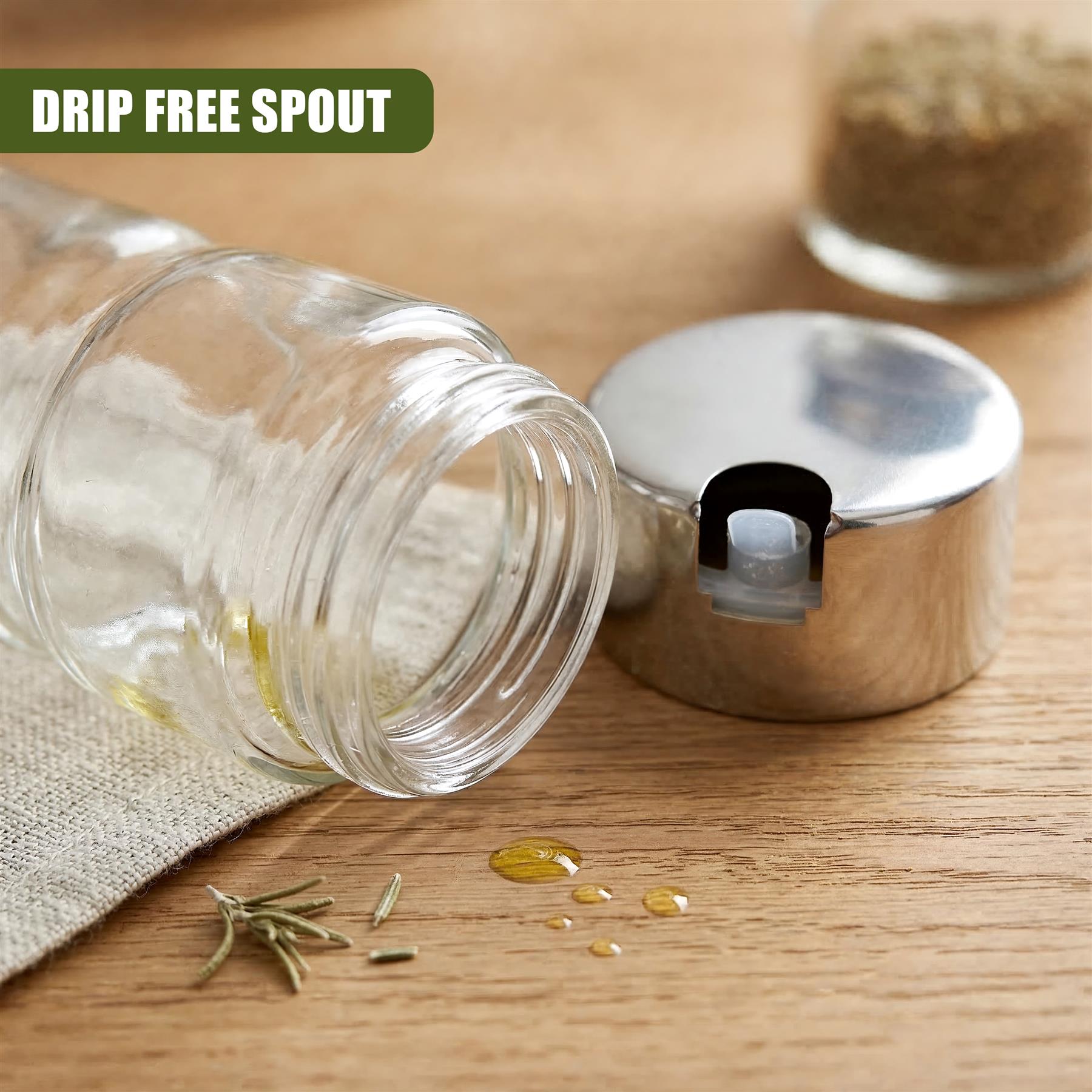 Clear glass bottle and metal spout unit displayed with scattered herbs and spices on wood.