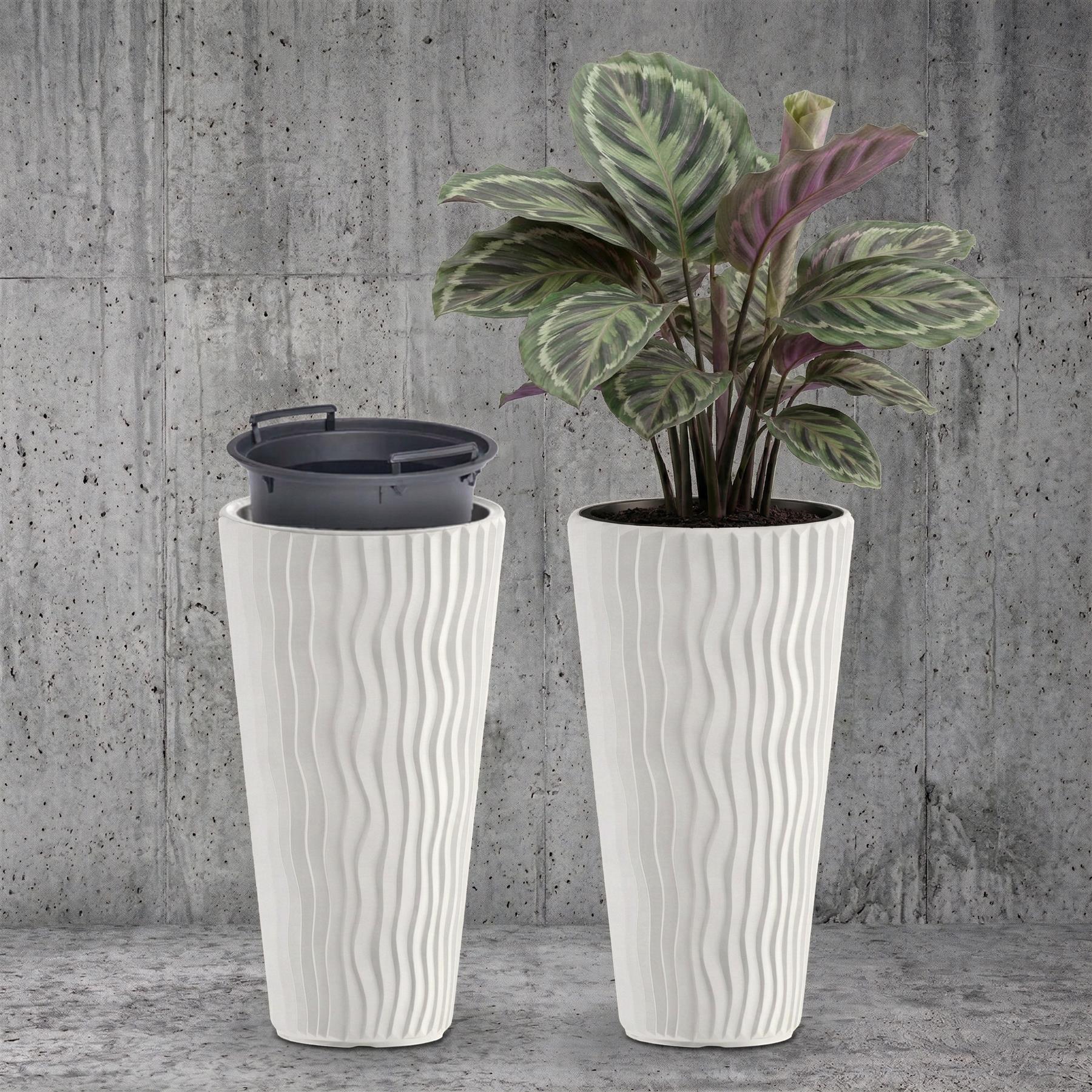 Two ribbed white pots rest on a gray surface, one holding a houseplant and one empty.