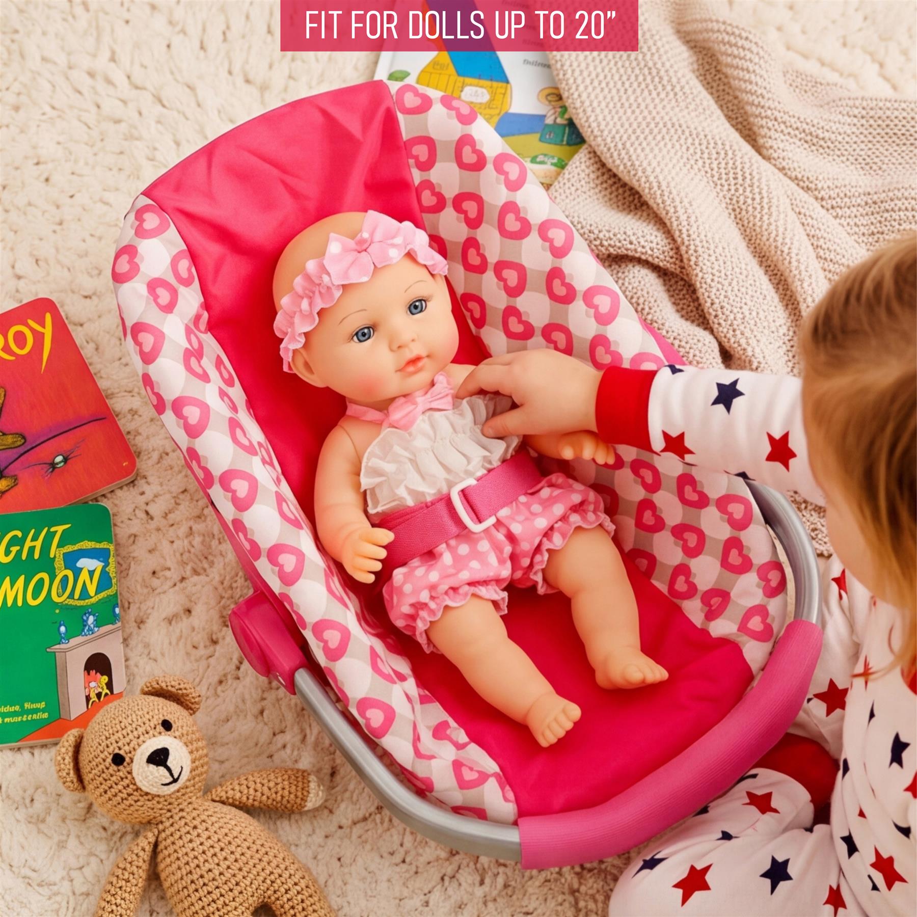 A baby doll is seated in a pink patterned car seat, being adjusted by a child's hand.