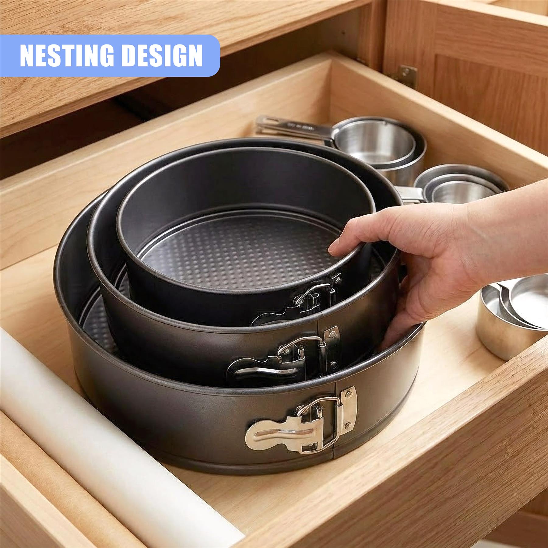 Stacked metal springform cake pans with latches resting inside a wooden kitchen drawer.