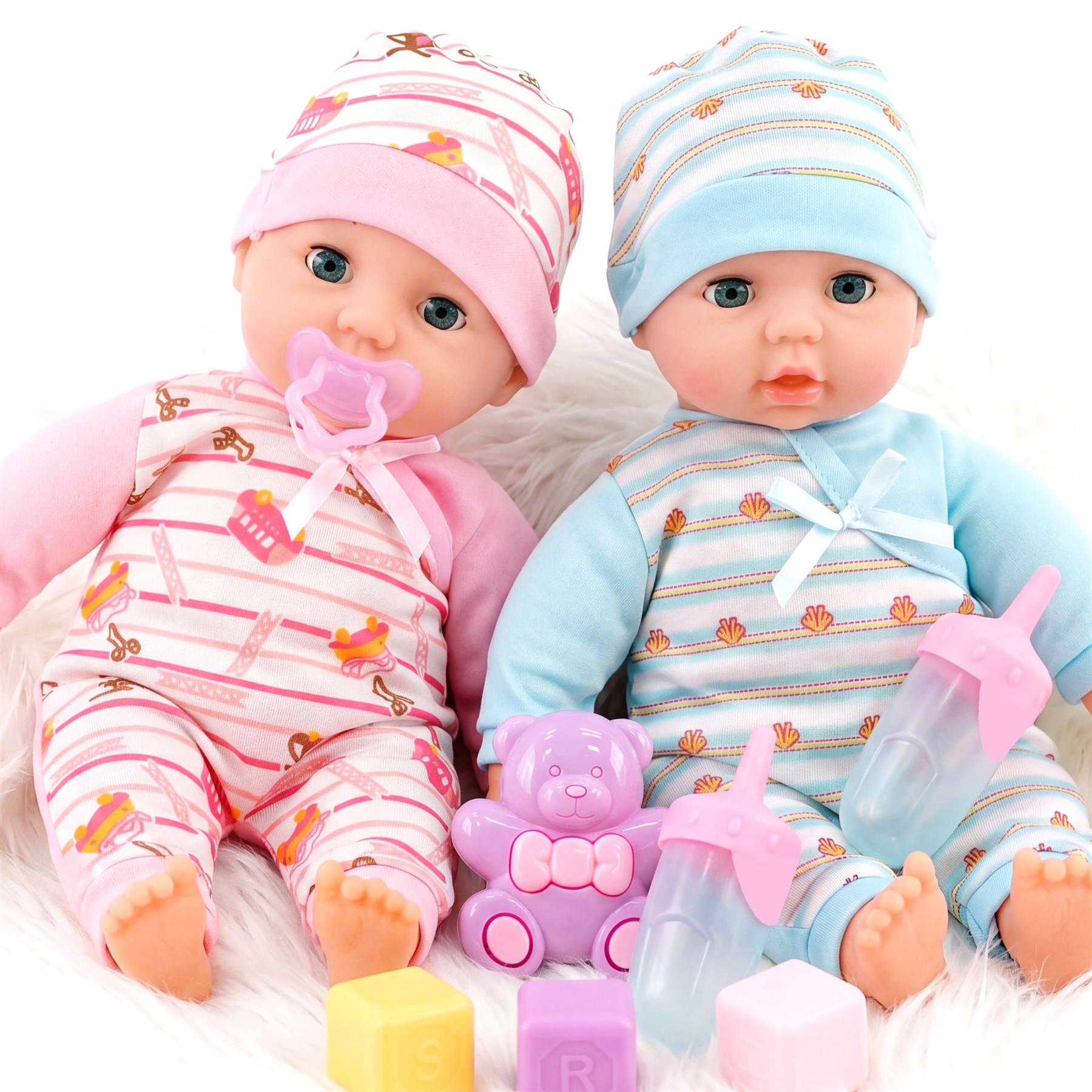 Two dolls in striped pajamas are surrounded by toy bottles, colorful blocks, and accessories.