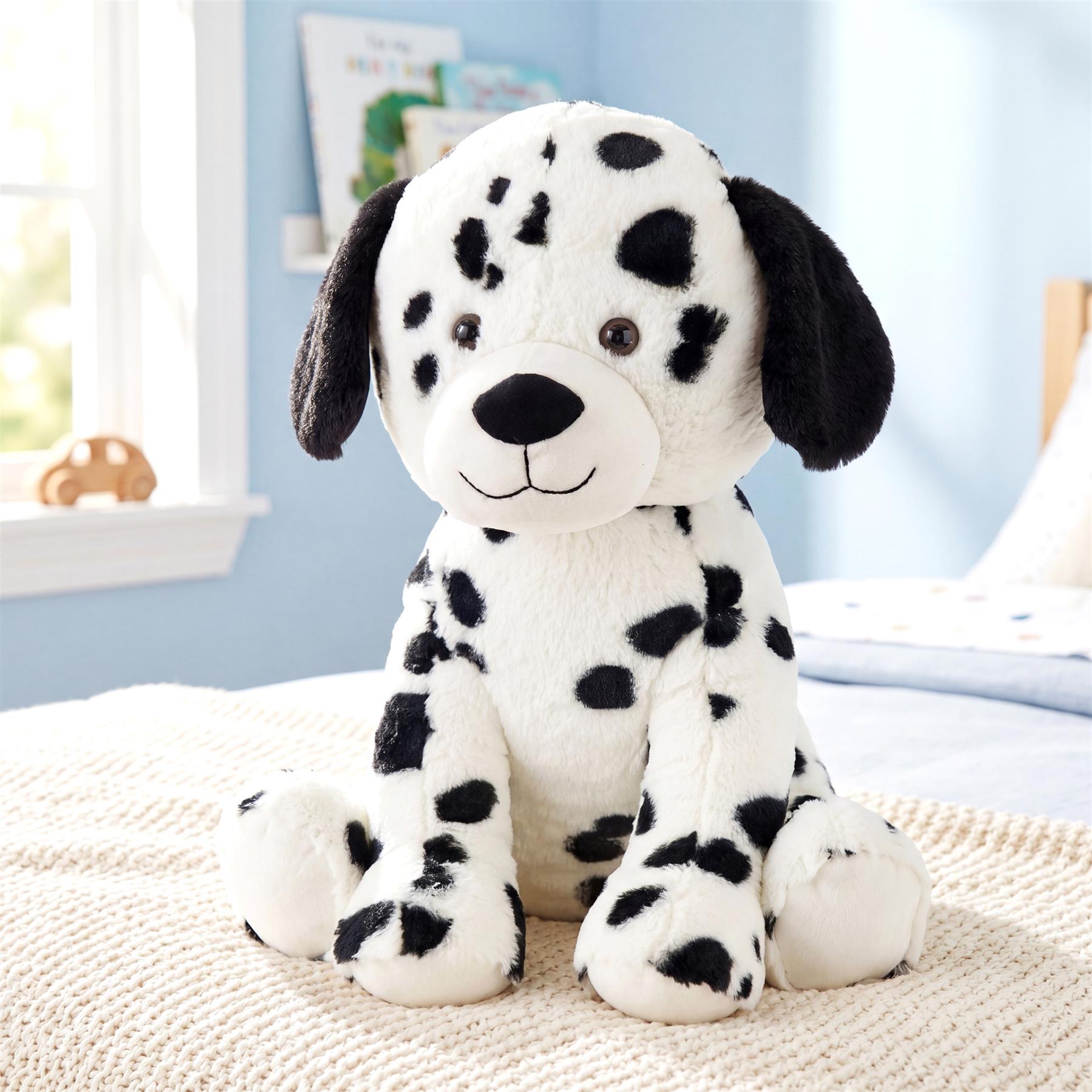 Fluffy stuffed Dalmatian toy with black spots sits on a textured cream blanket.