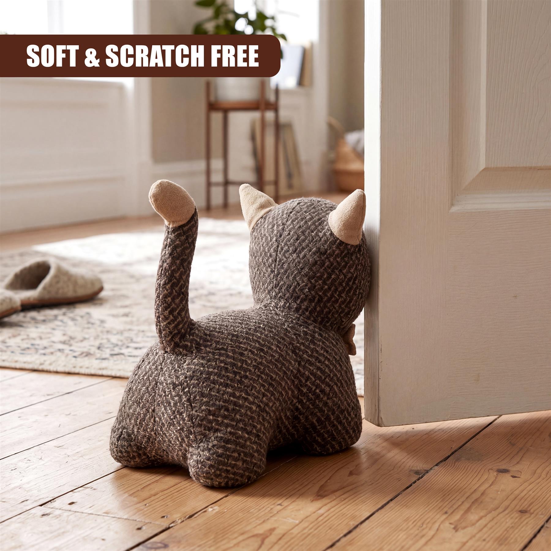 Knitted kitten door stopper rests against a white door frame on a wooden floor.
