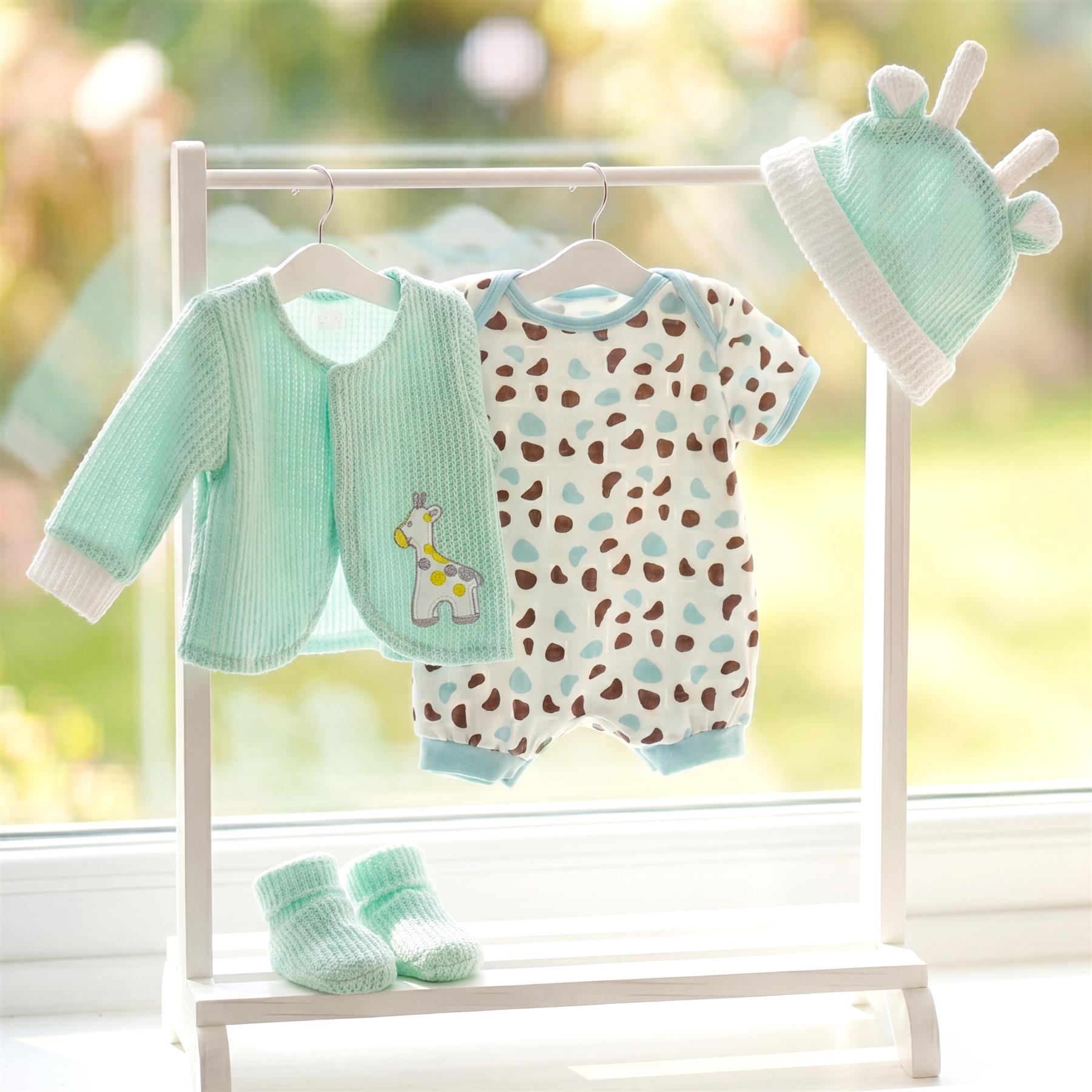White clothes rack displaying mint green jacket, spotted outfit, hat, and small booties.