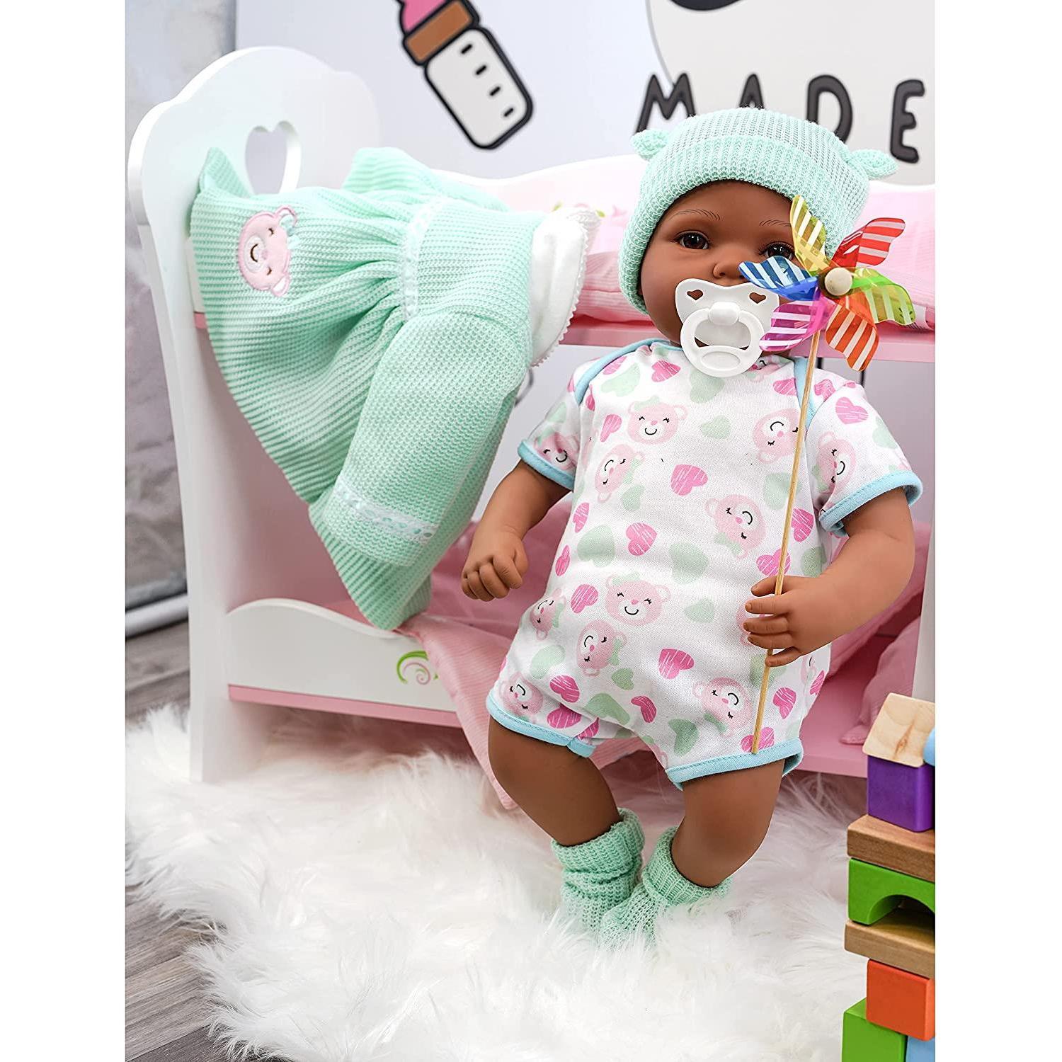 This is a baby doll with a dress and sitting on top of a doll house bed, holding a flag in front of her. The doll house bed has pink bedding, and the room where the photo was taken looks like a nursery or child's bedroom. - The Magic Toy Shop