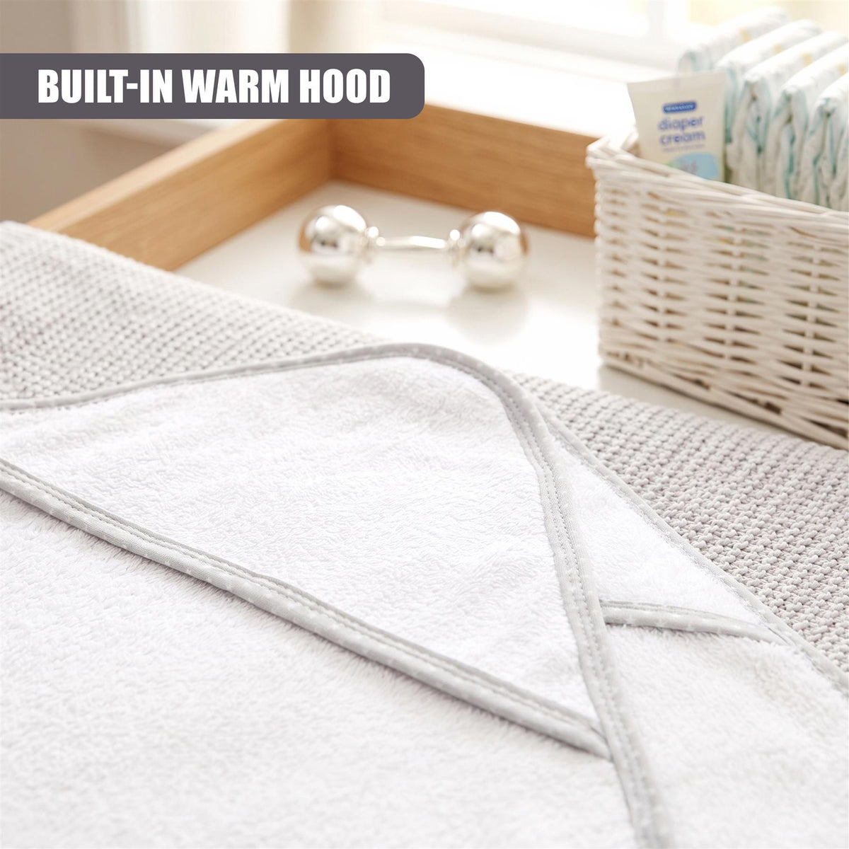 Grey GEEZY hooded baby bath towel set, featuring a built-in warm hood, sits on a wooden tray with diapers and baby wipes