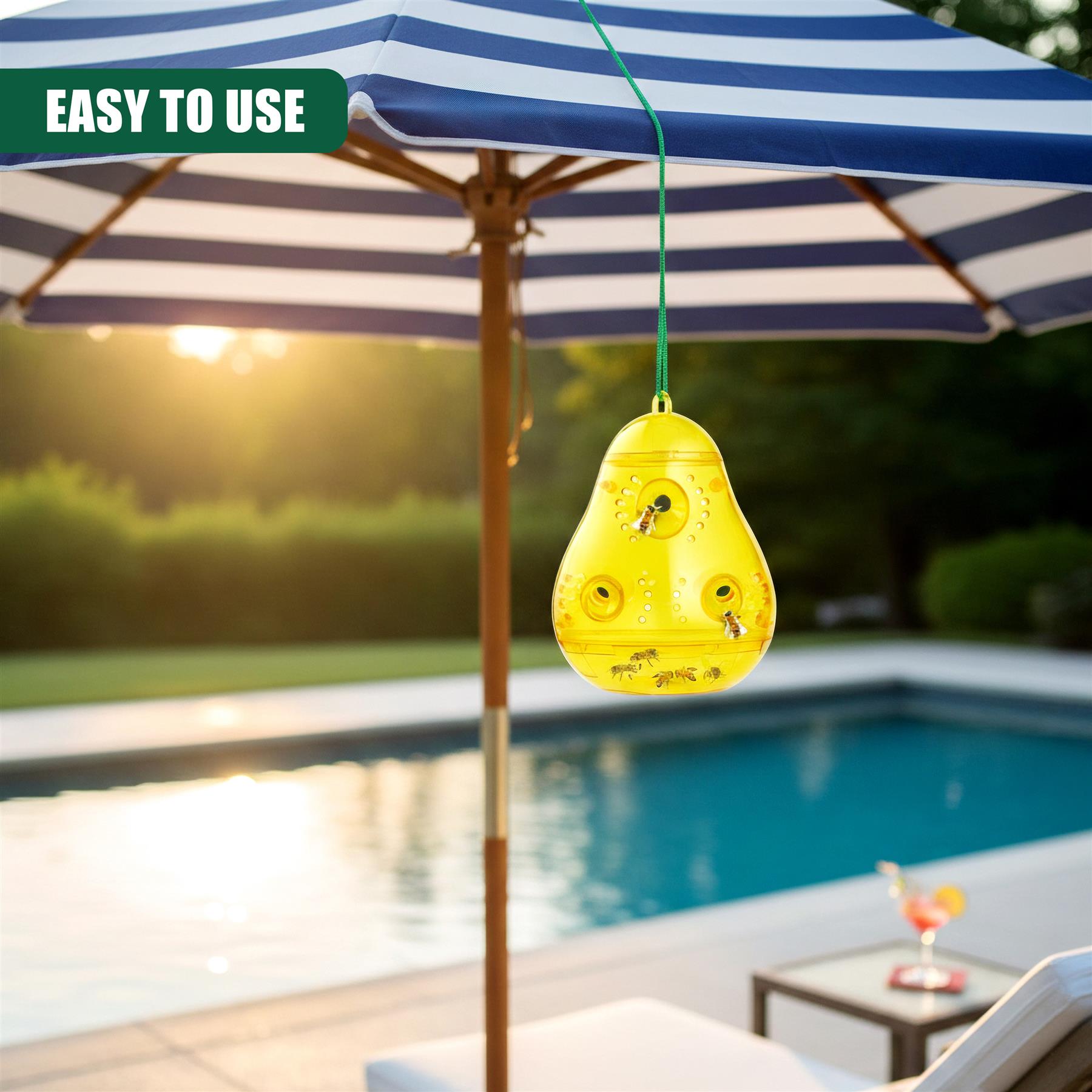 Yellow wasp trap hangs from a striped umbrella near a swimming pool.