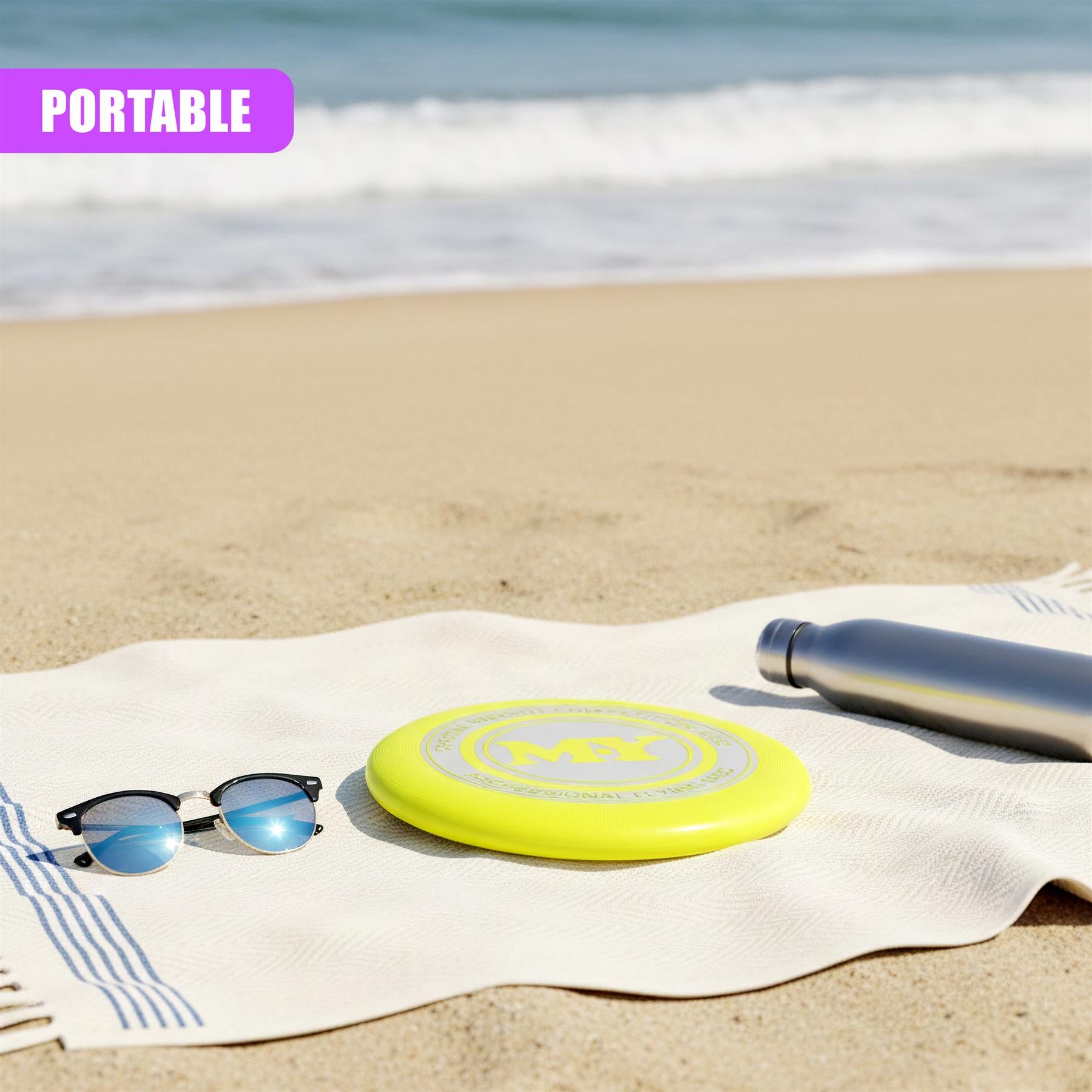 Yellow professional frisbee rests on a beach towel next to sunglasses and a water bottle.