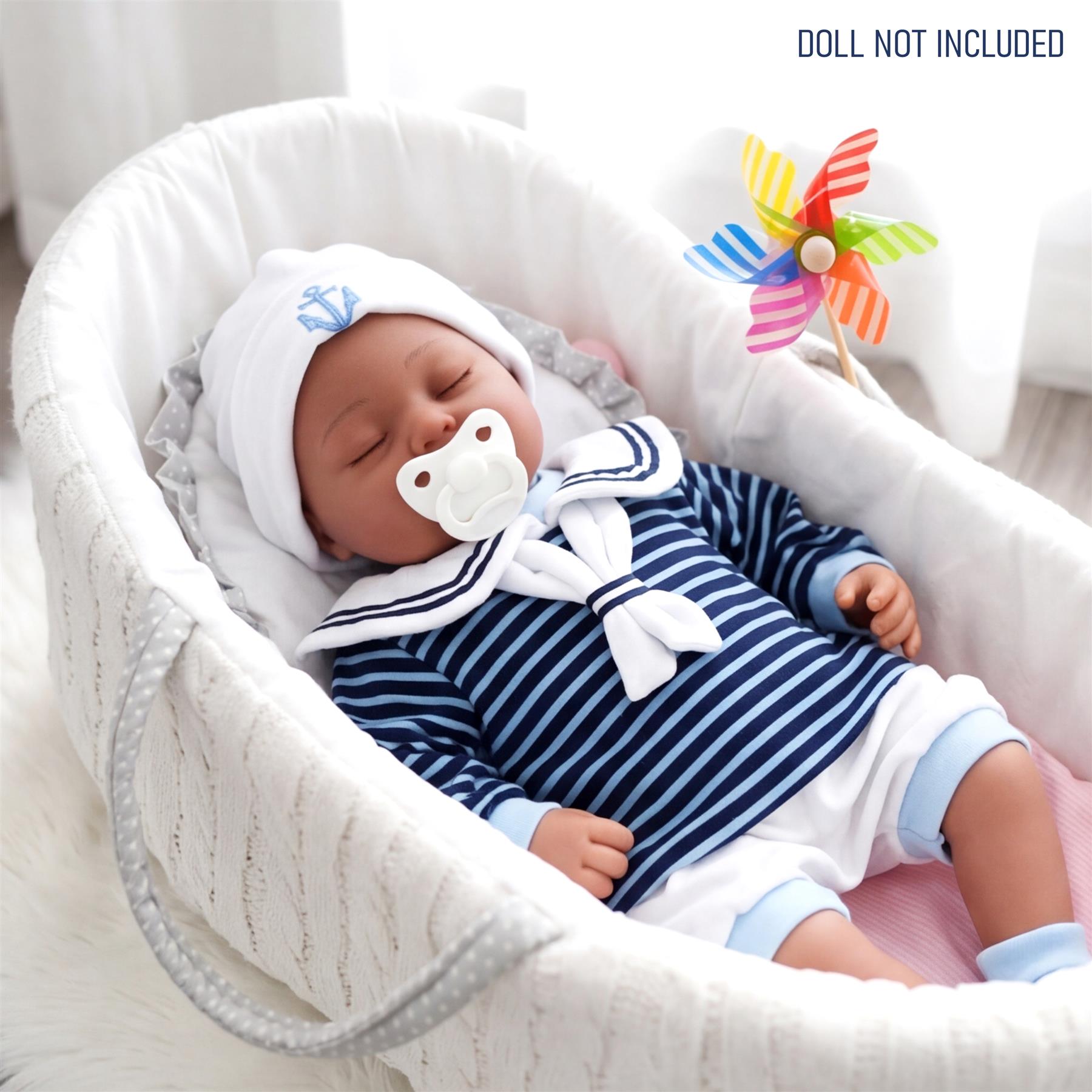 A doll dressed in navy and white striped sailor outfit, lying peacefully in a white bassinet.