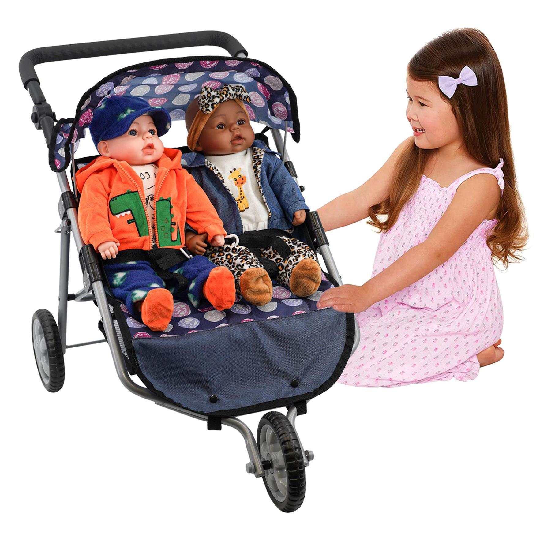 Girl stands beside a blue three-wheeled pushchair containing two seated toy dolls.