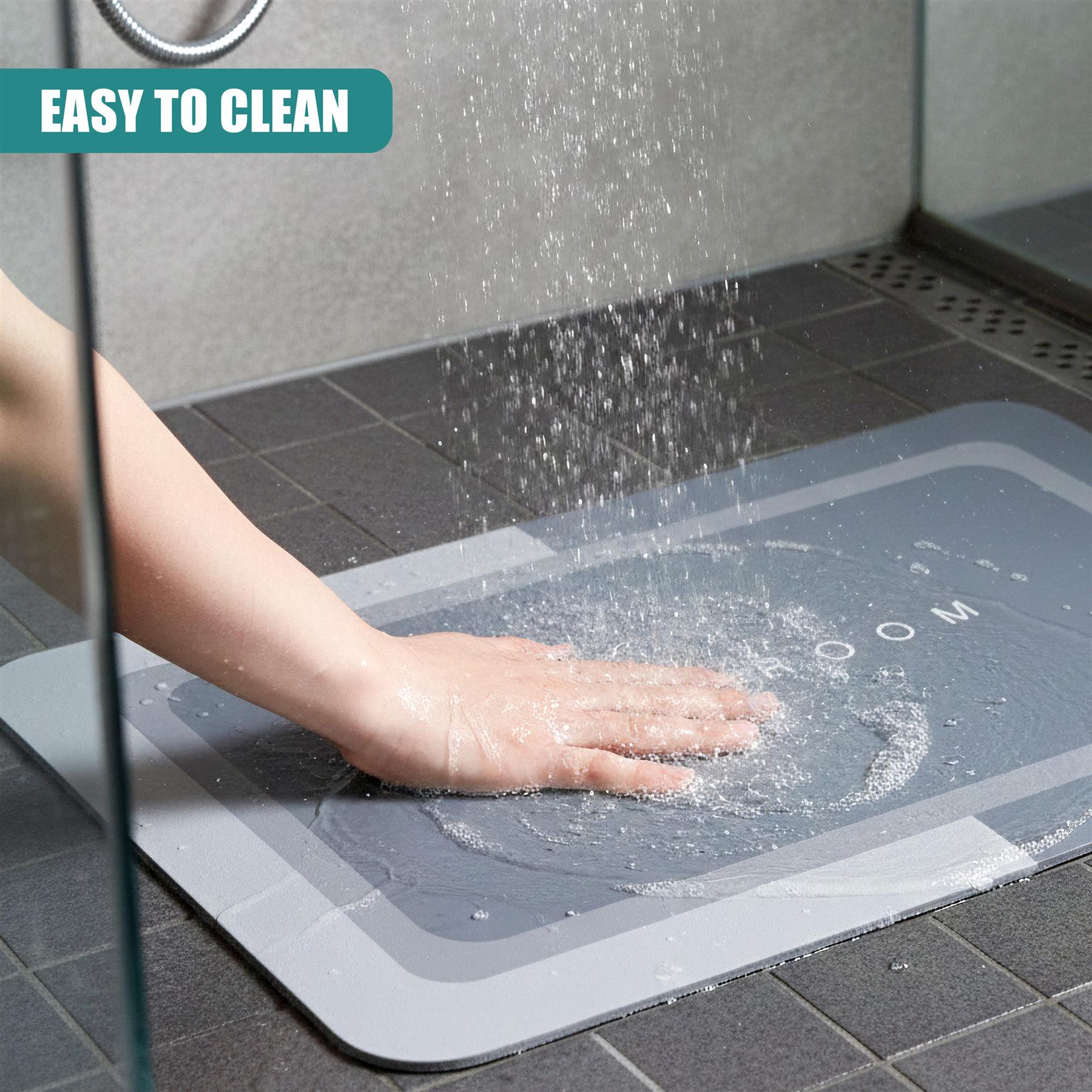 A hand washes a grey anti-slip bathroom mat surface under running water in a tiled area.