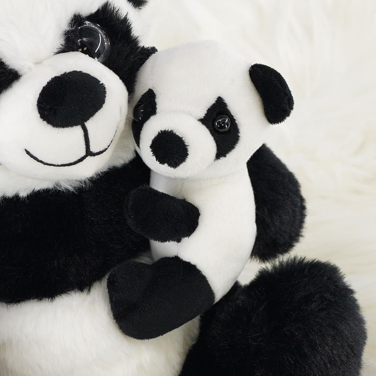 A large, super soft panda plush toy embraces a smaller panda plush toy, both featuring black and white fur and cheerful expressions. The background is a soft, fluffy white material, emphasizing the cuddliness of the toys. Perfect for stuffed animal lovers. themagictoyshop