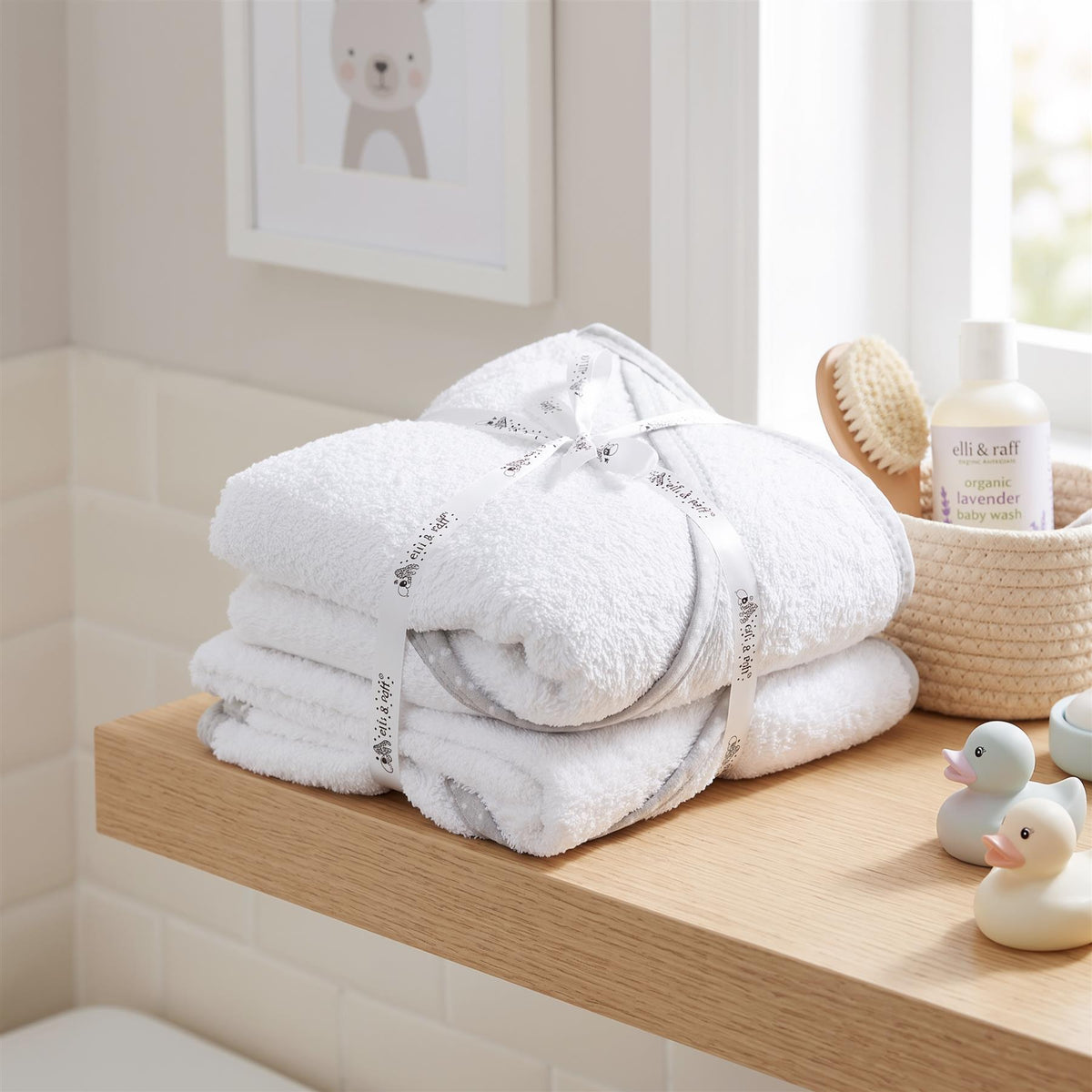 Pack of 2 GEEZY hooded baby bath towels stacked on a wooden shelf with baby bath toys