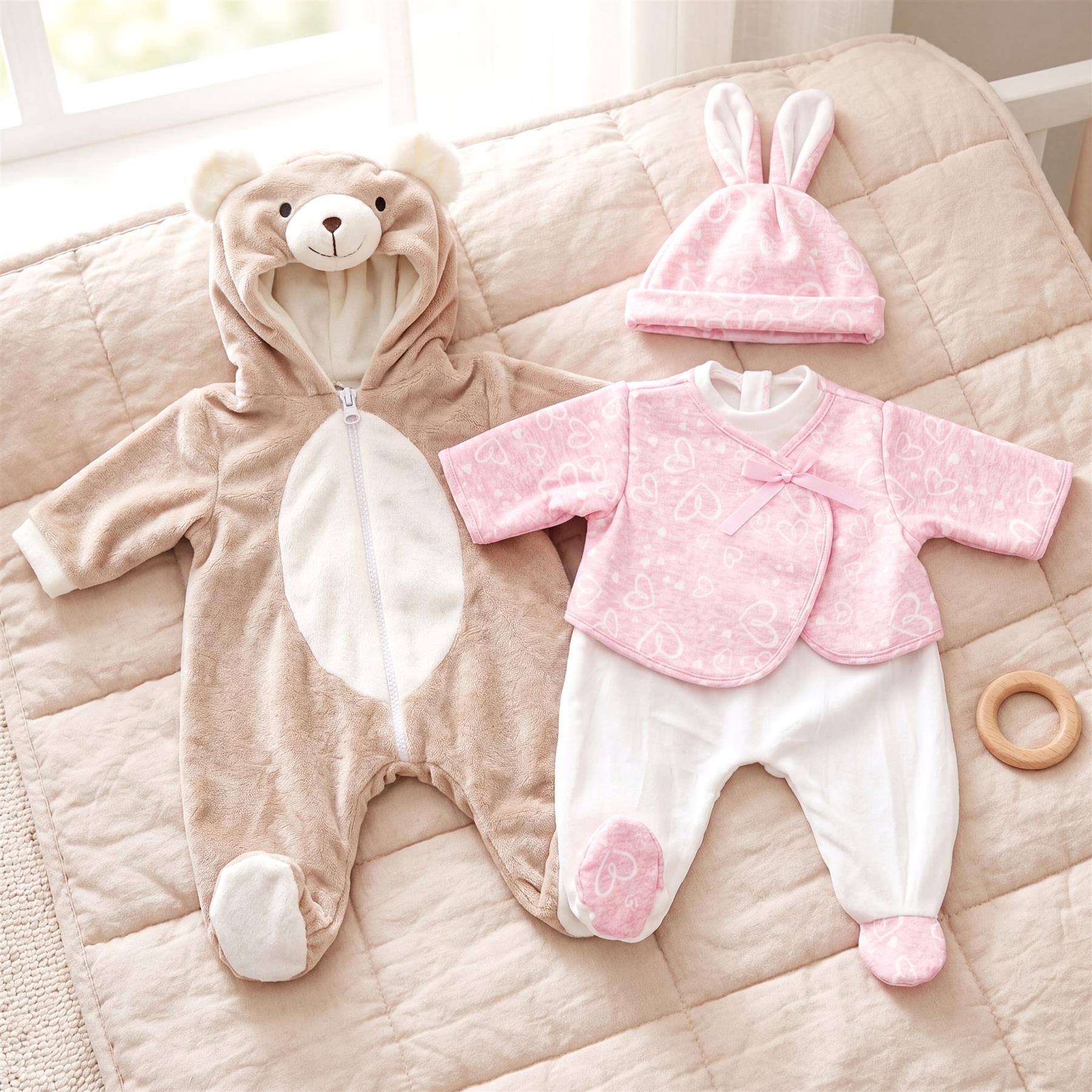 A bear hooded romper and pink bunny top and pants set are displayed on a neutral surface.