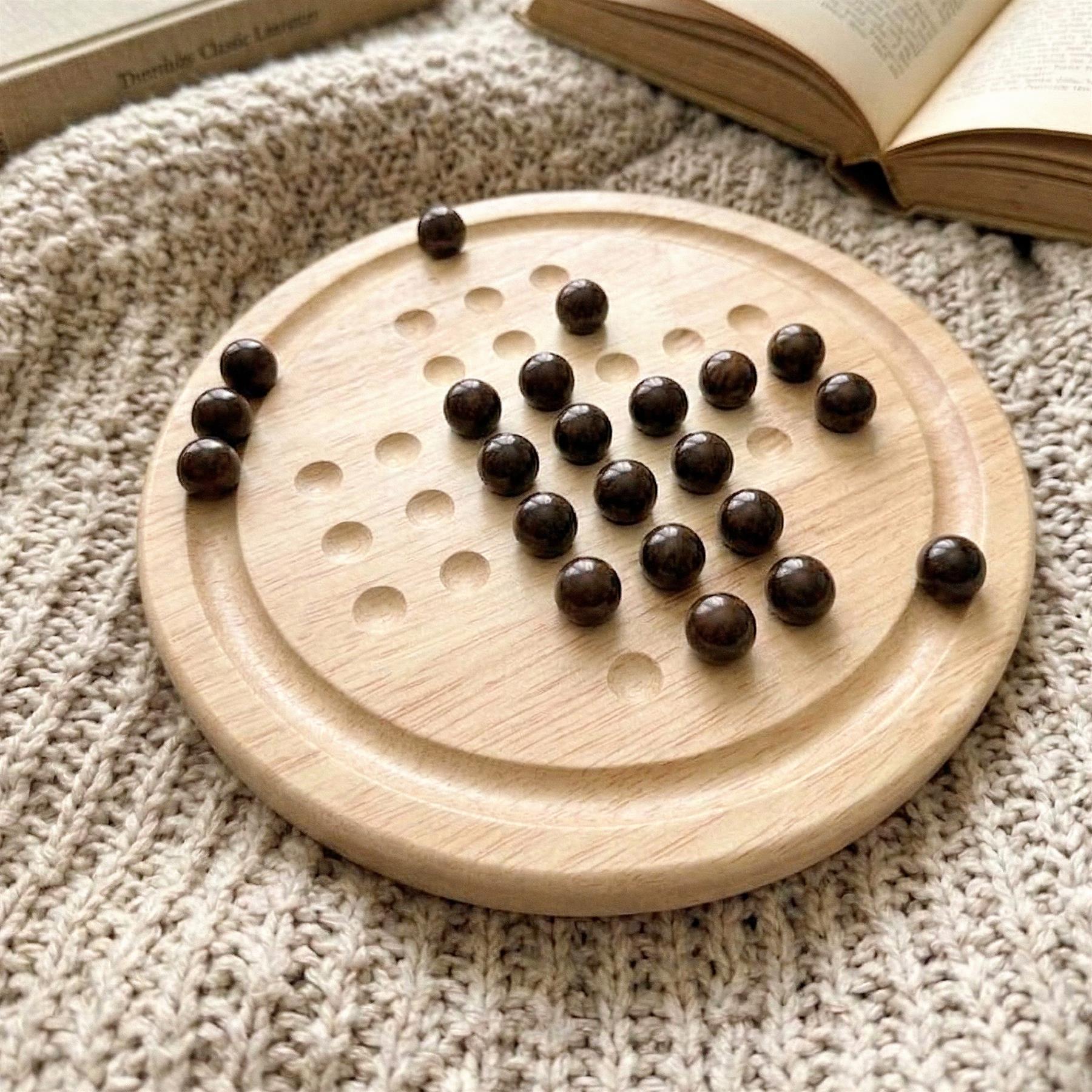 Light wooden board game with drilled holes and multiple scattered dark brown circular pieces.