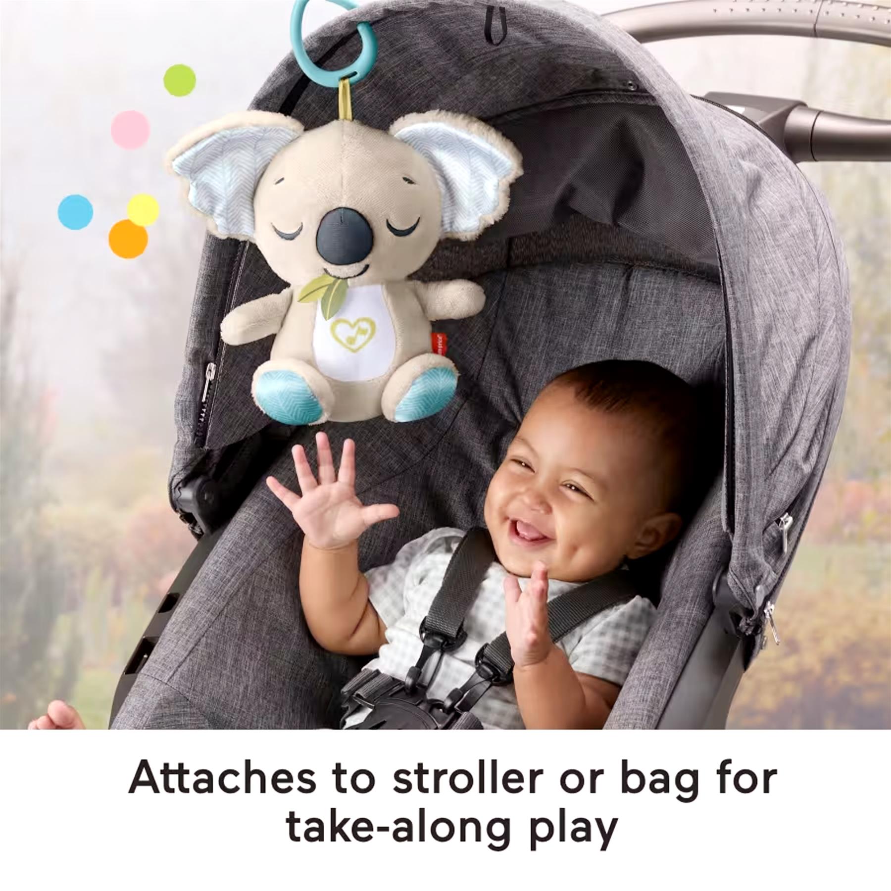 Plush koala soother hangs from the stroller while a baby smiles inside the carrier.