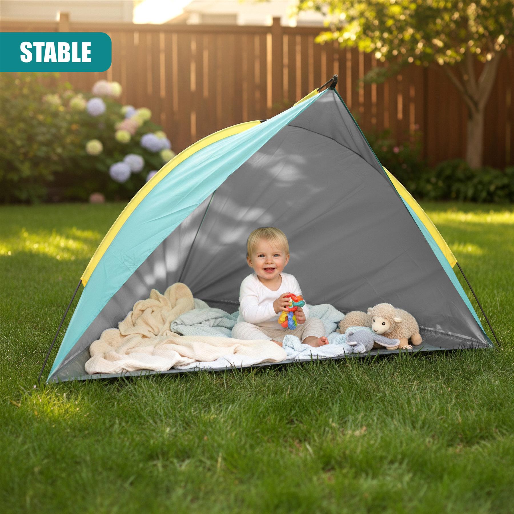 Child sitting inside a pop-up beach tent on green grass with stuffed toys visible.
