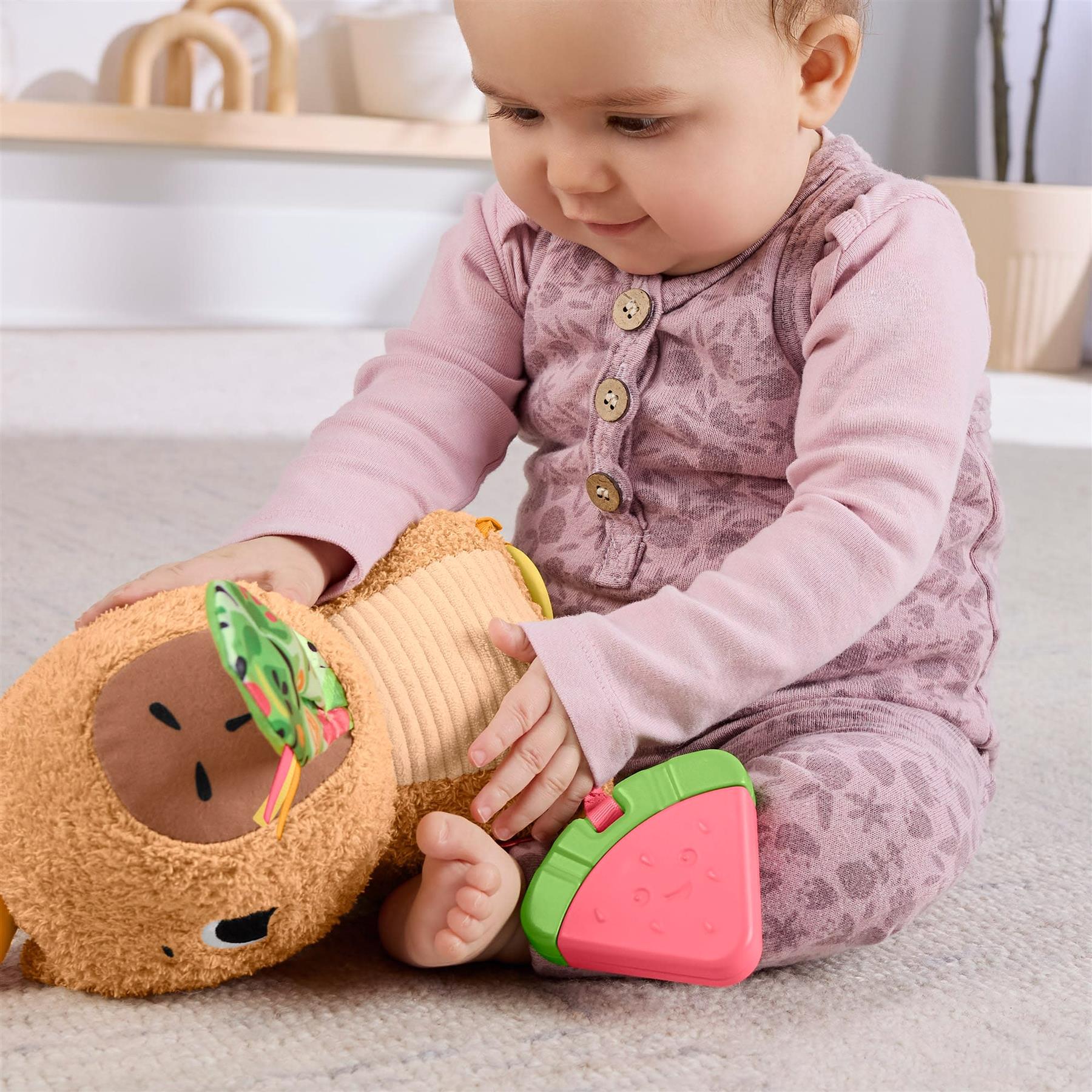 Baby plays with a plush brown capybara toy and a bright pink and green sensory snack piece.