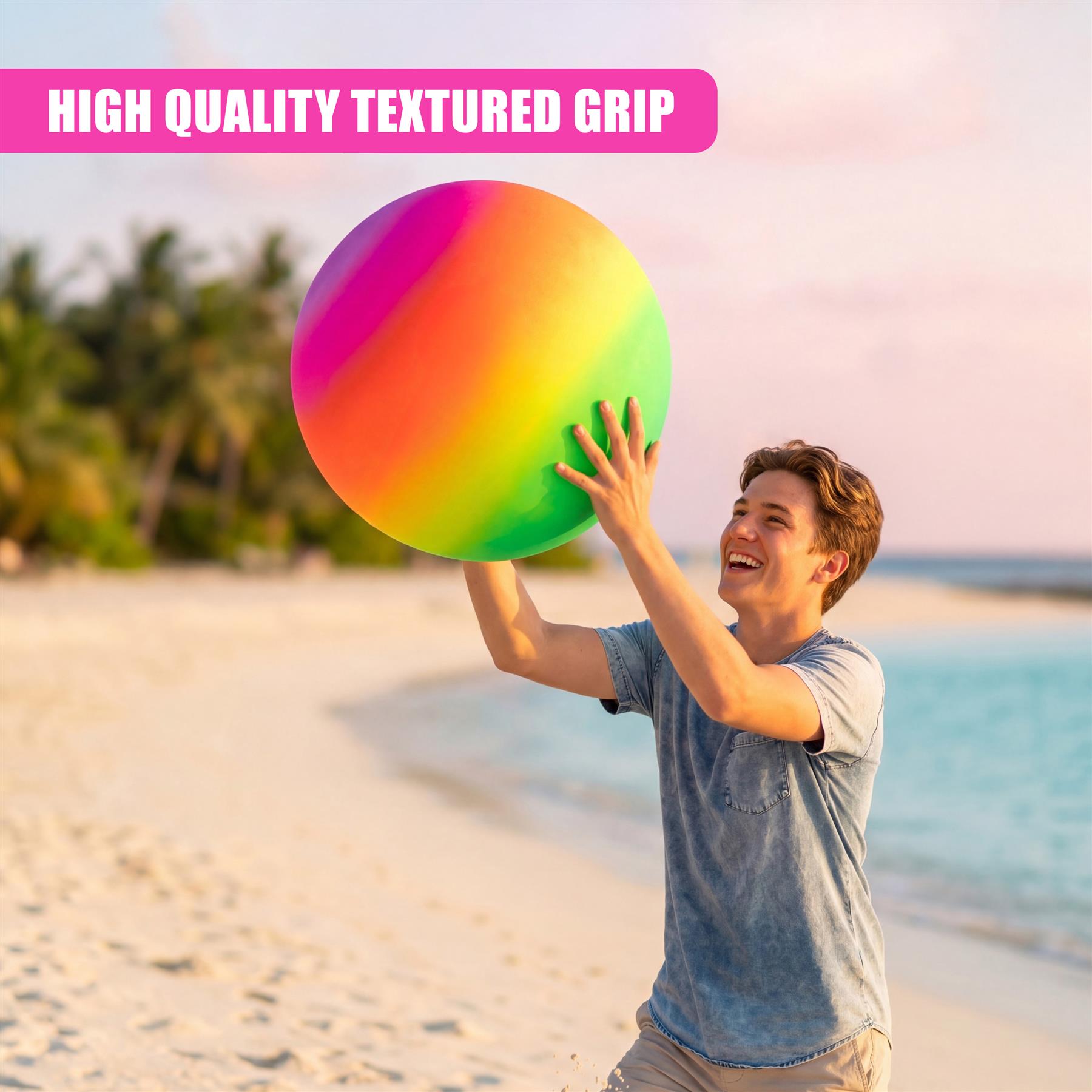 A young man standing on a beach holding a large, bright rainbow-colored ball.