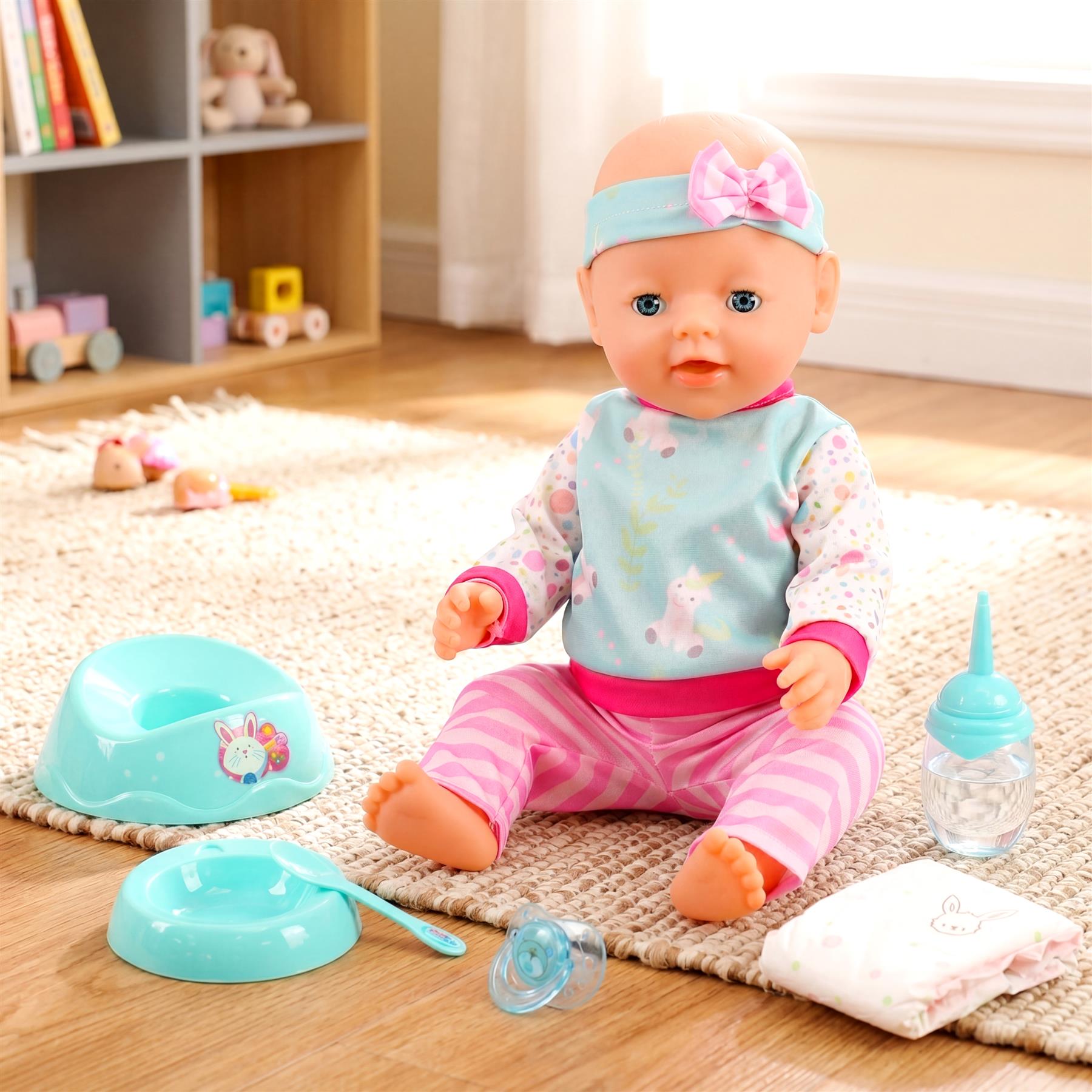 Doll wearing patterned clothes sits with blue bowls, bottle, and pink cloth accessories.