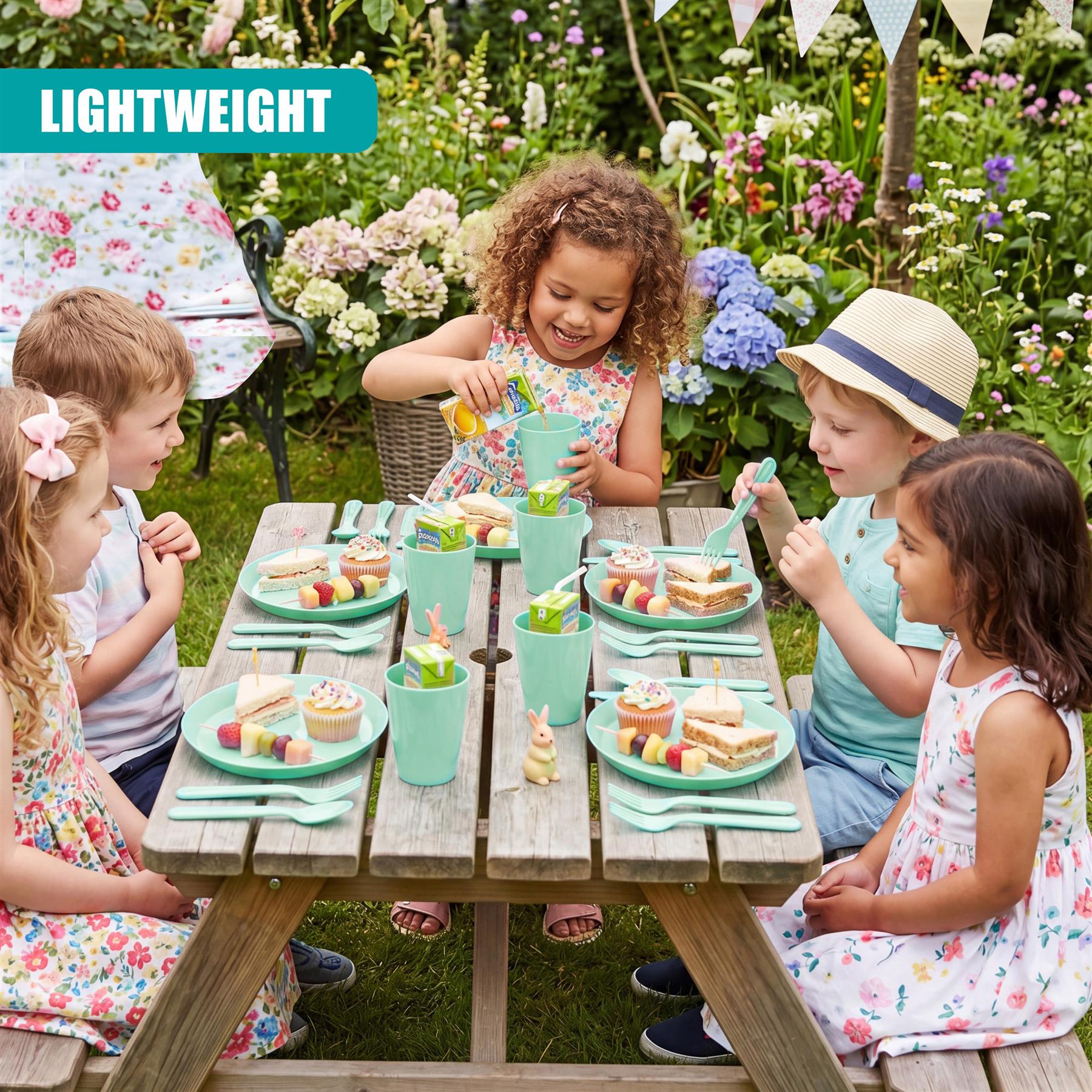 Children sit at a wooden table using green plastic dishes for an outdoor picnic setting.