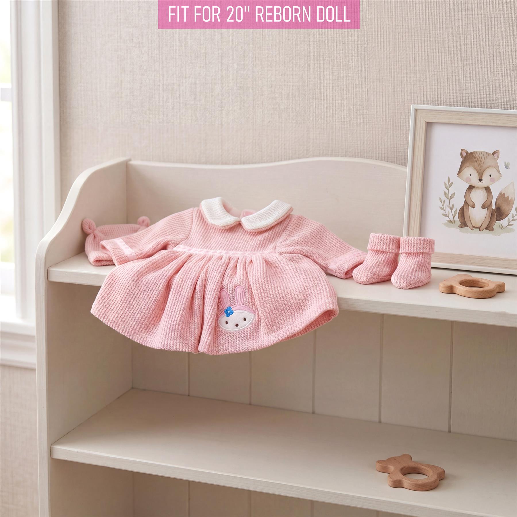 Knitted pink doll dress features a white collar and small graphic detail, displayed with matching knitted accessories.
