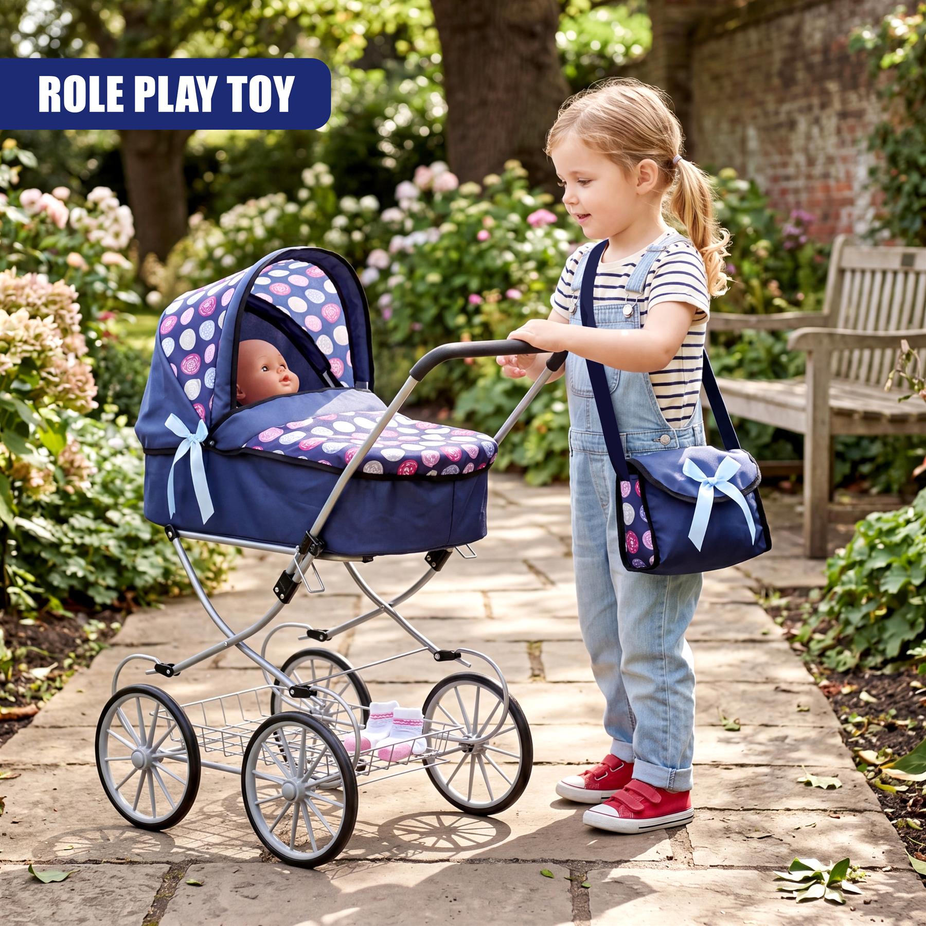 A girl in overalls stands beside a blue and white toy pram on a garden path.