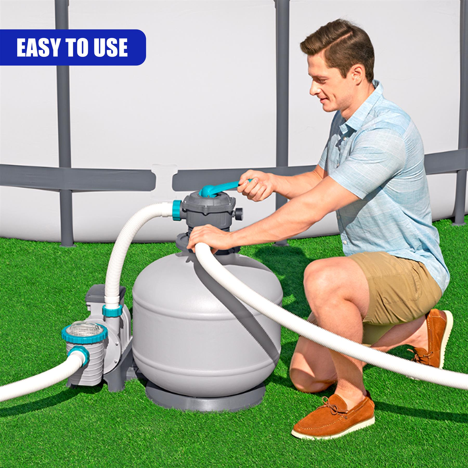 A man is kneeling beside a large gray filter unit, adjusting the connected plumbing system.