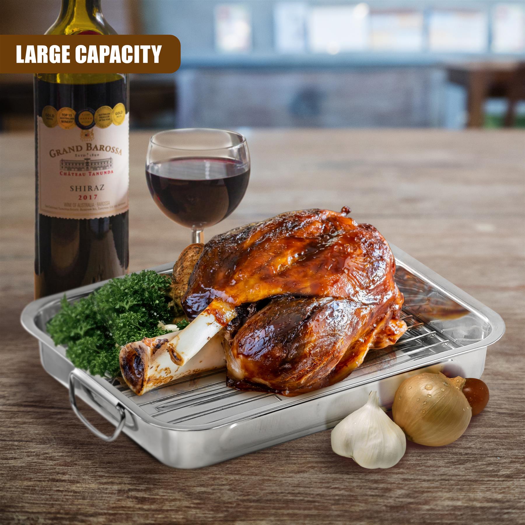 Roasted poultry and herbs rest on a silver metal roasting tray with a rack, near wine and garlic.