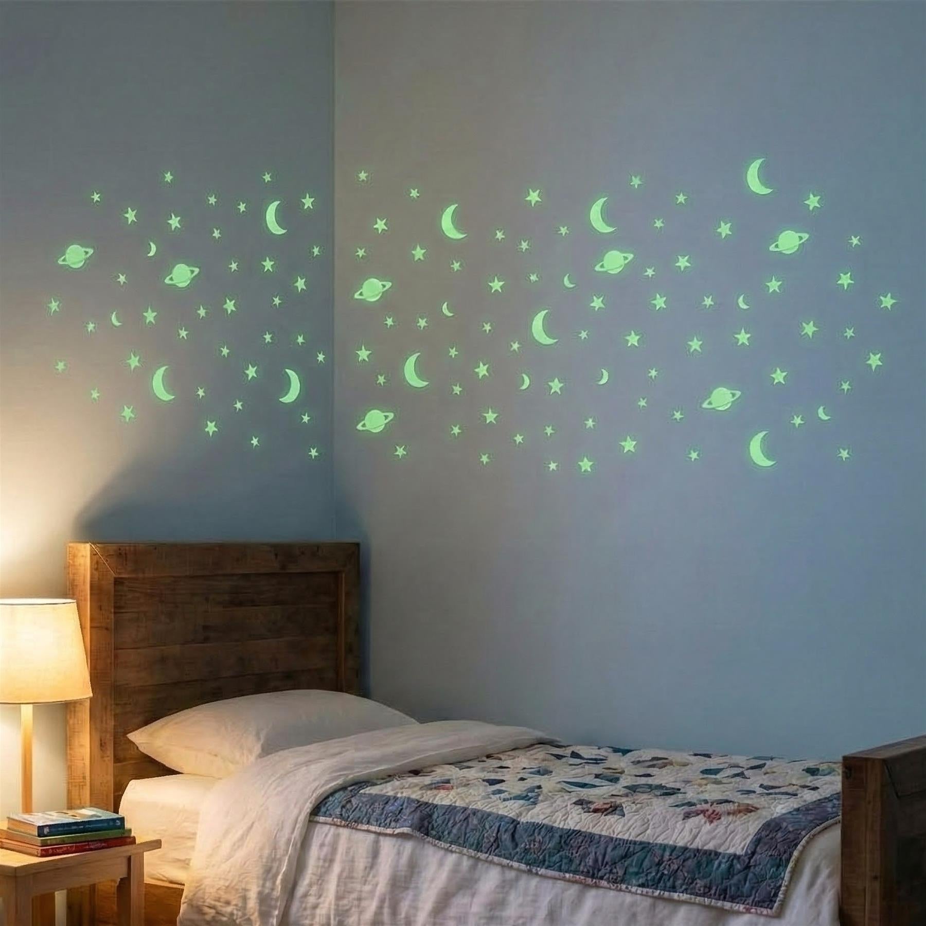 A bed in a child's bedroom, with a wooden headboard and a quilted bedspread. The wall above the bed is covered with a glow-in-the-dark stars and planets decal, featuring a variety of shapes and colors. - The Magic Toy Shop