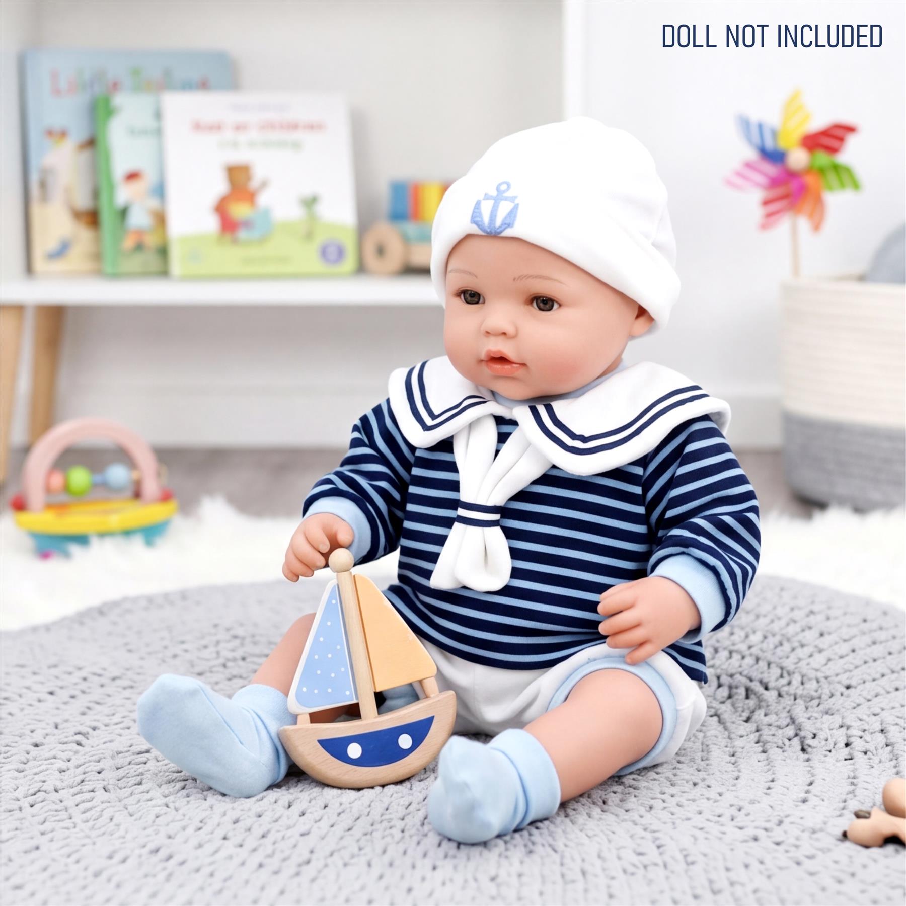 Reborn doll wearing a striped sailor outfit and hat, sitting with a small wooden toy boat.