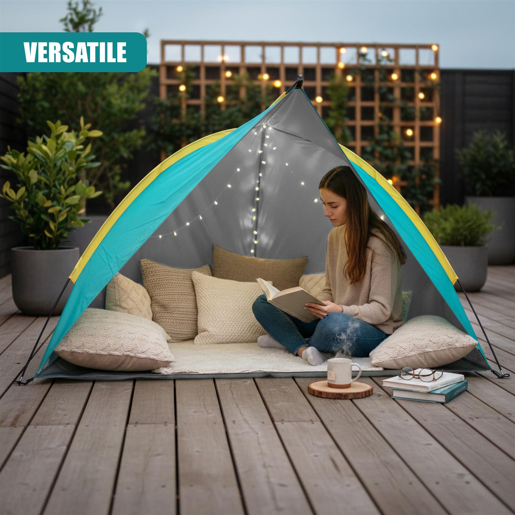 A woman reads a book inside a pop-up tent on a deck with cushions, potted plants, and stacked books.