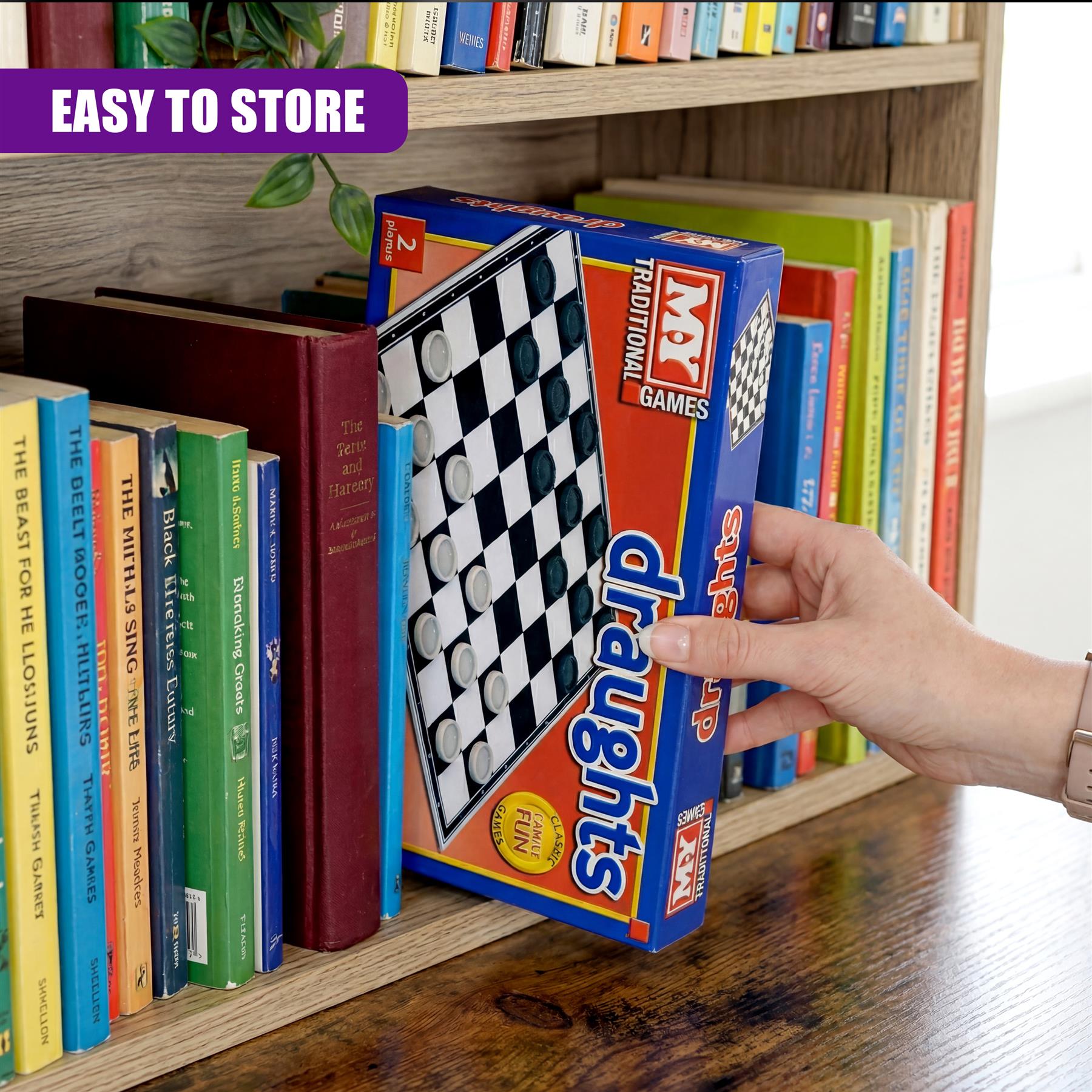 The folding draughts game box featuring black and white squares rests on a wooden surface near books.