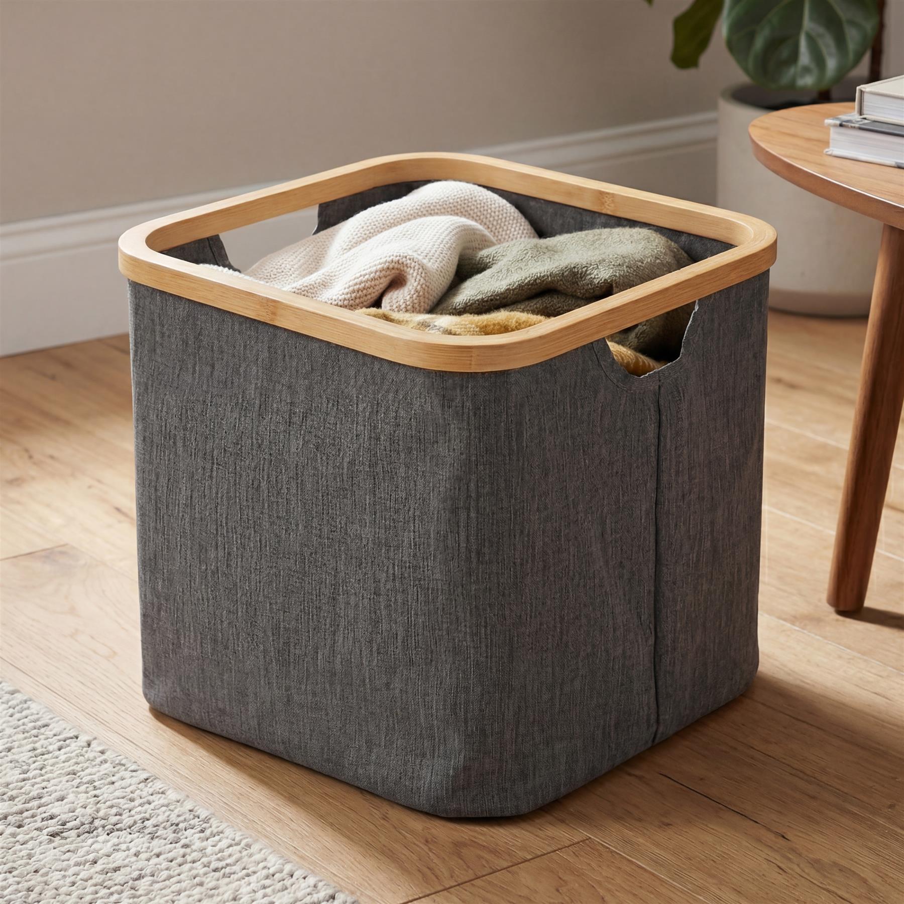 Gray fabric hamper with a wooden rim sits on a floor, filled with folded light-colored textiles.