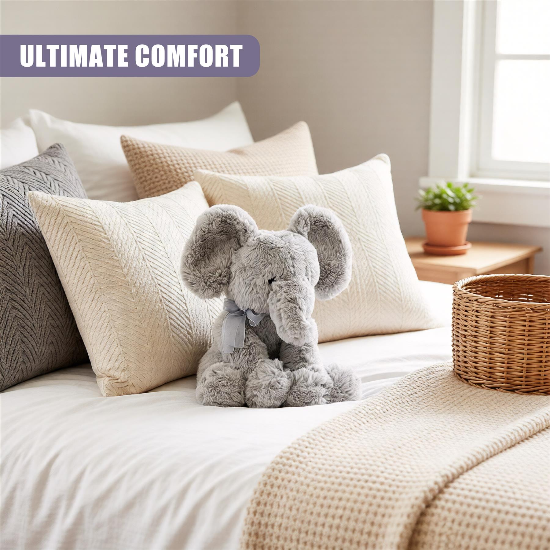 Grey plush stuffed elephant toy sits on a neutral-toned bed among pillows and blanket.