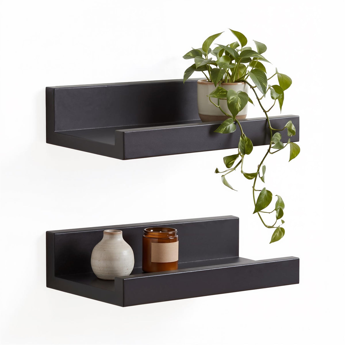Two black GEEZY floating shelves display a plant and a candle on a white wall