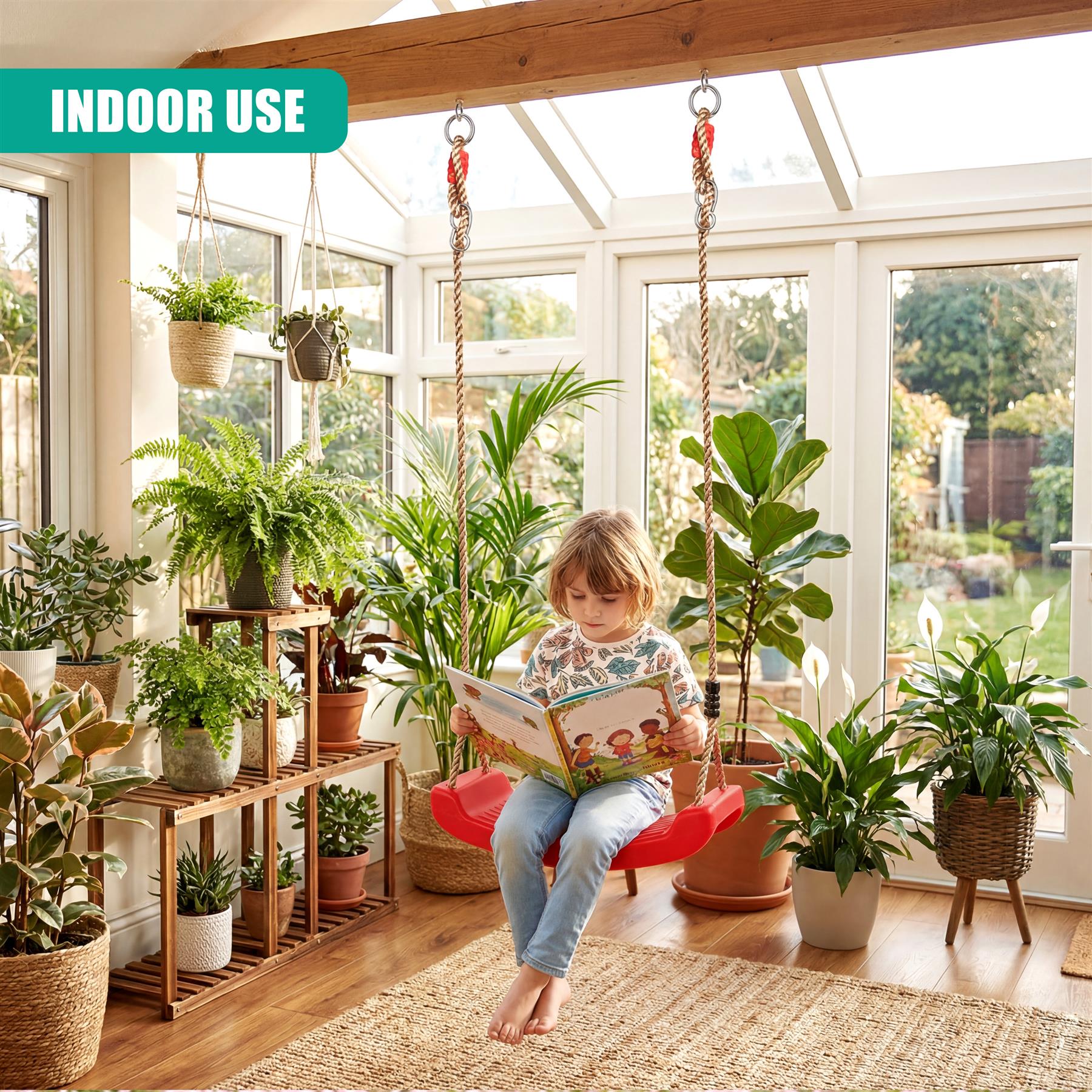 Child reads a book while sitting on a red swing in a room surrounded by lush tropical plants.