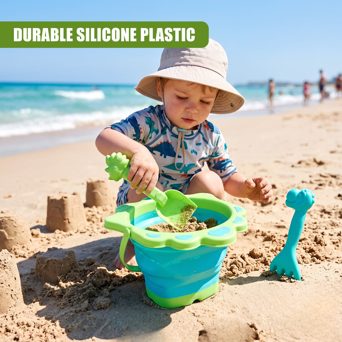 A young boy plays with a green and blue collapsible beach bucket and spade set on a sandy beach