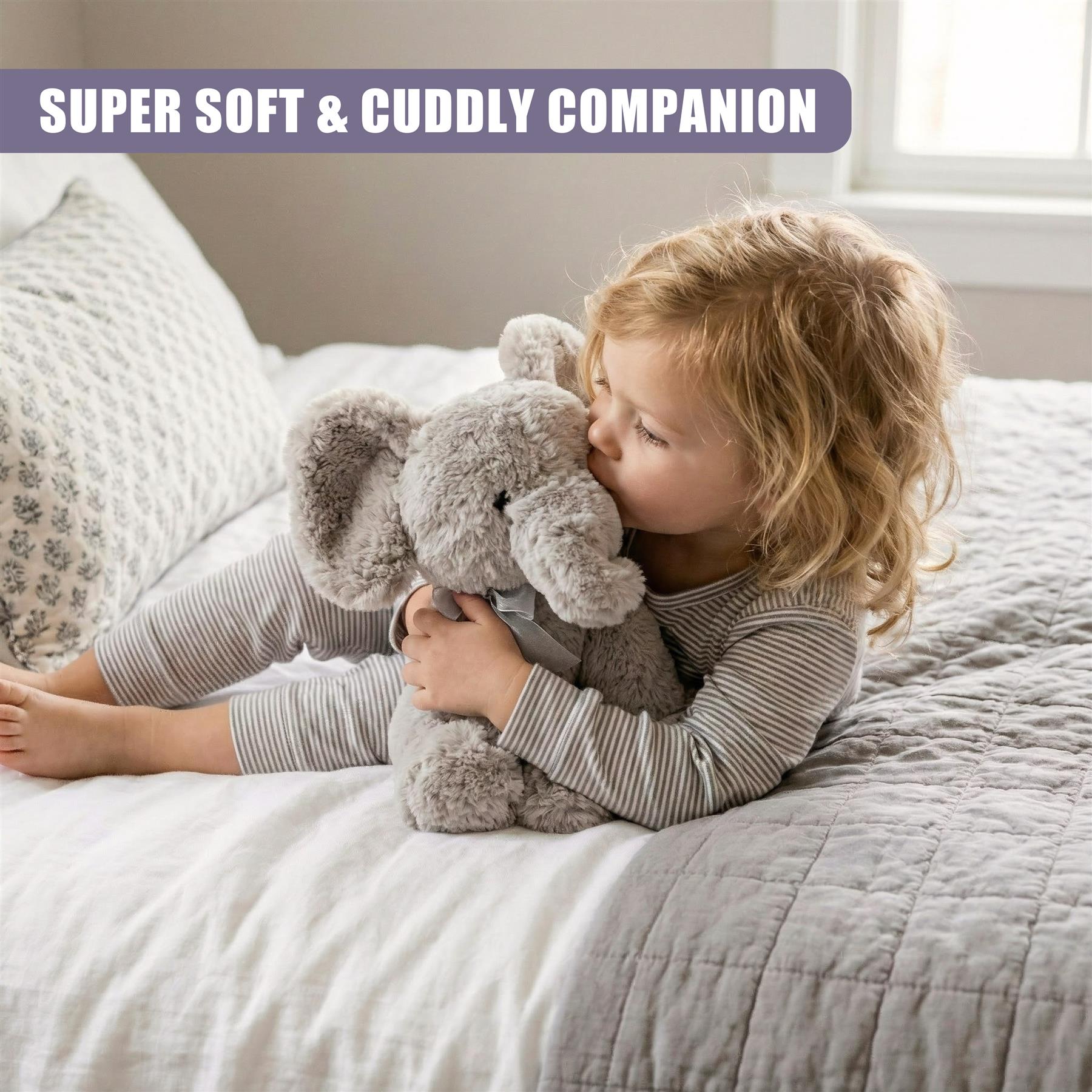 Young child lying on a bed, hugging a plush grey elephant stuffed toy.