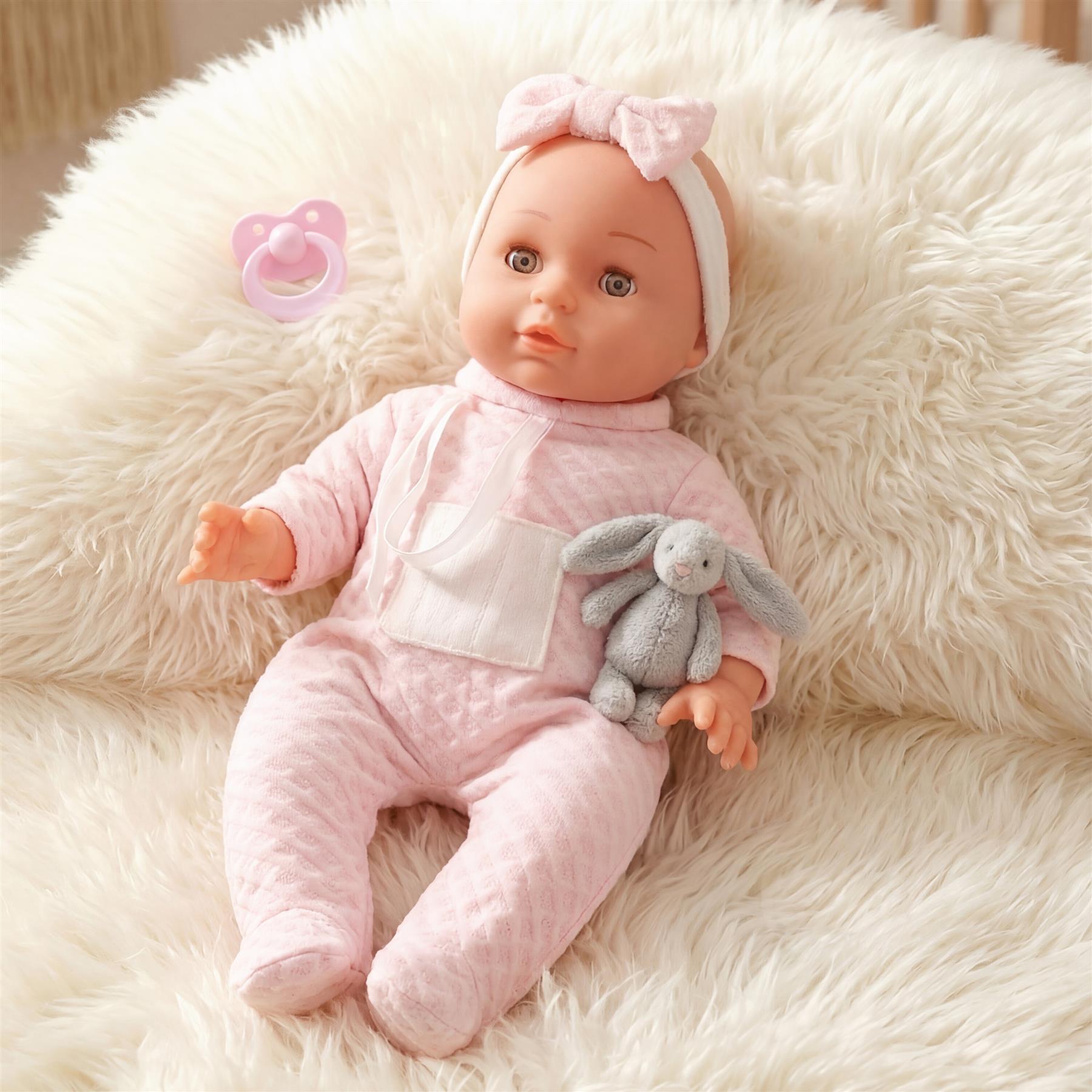 Pink doll in a pink outfit, resting on a cream rug with a small stuffed bunny toy.
