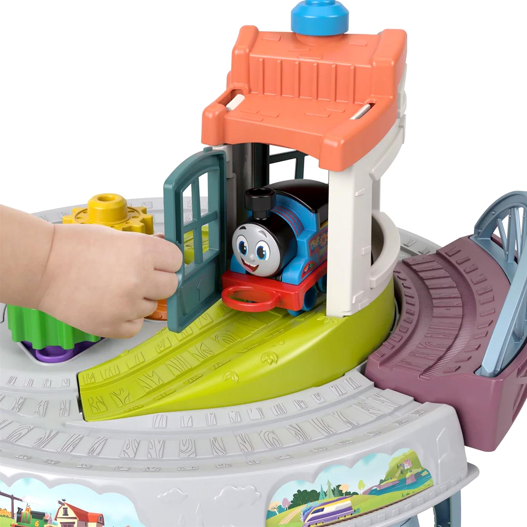 The table shows a blue train, green tracks, and a red station structure being played with by a hand.