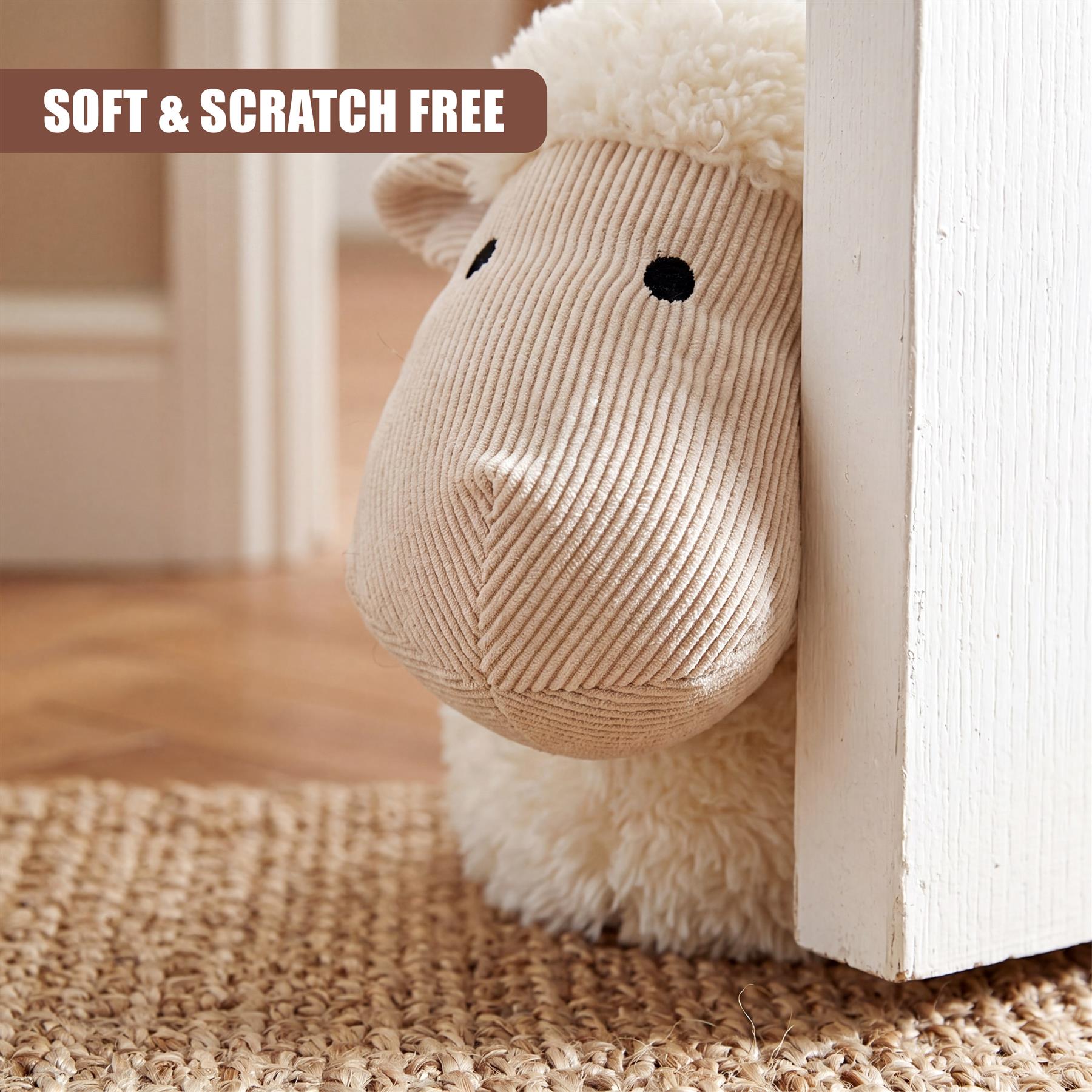 A fluffy stuffed sheep door stopper rests against a white door frame on a woven natural fiber rug.