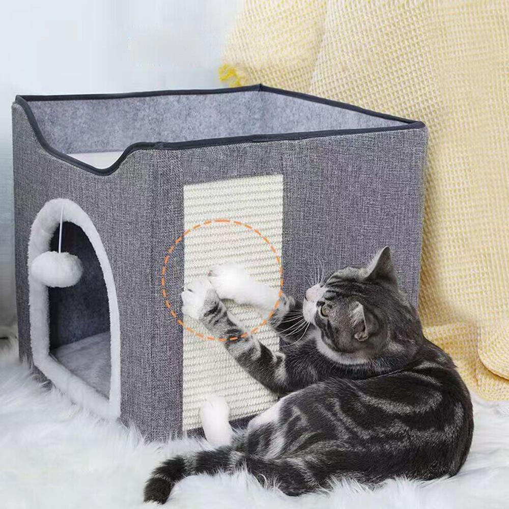 A cat plays with a toy in front of a grey, fabric cat house with a window, a door, and a ball of yarn hanging from the roof. - The Magic Toy Shop